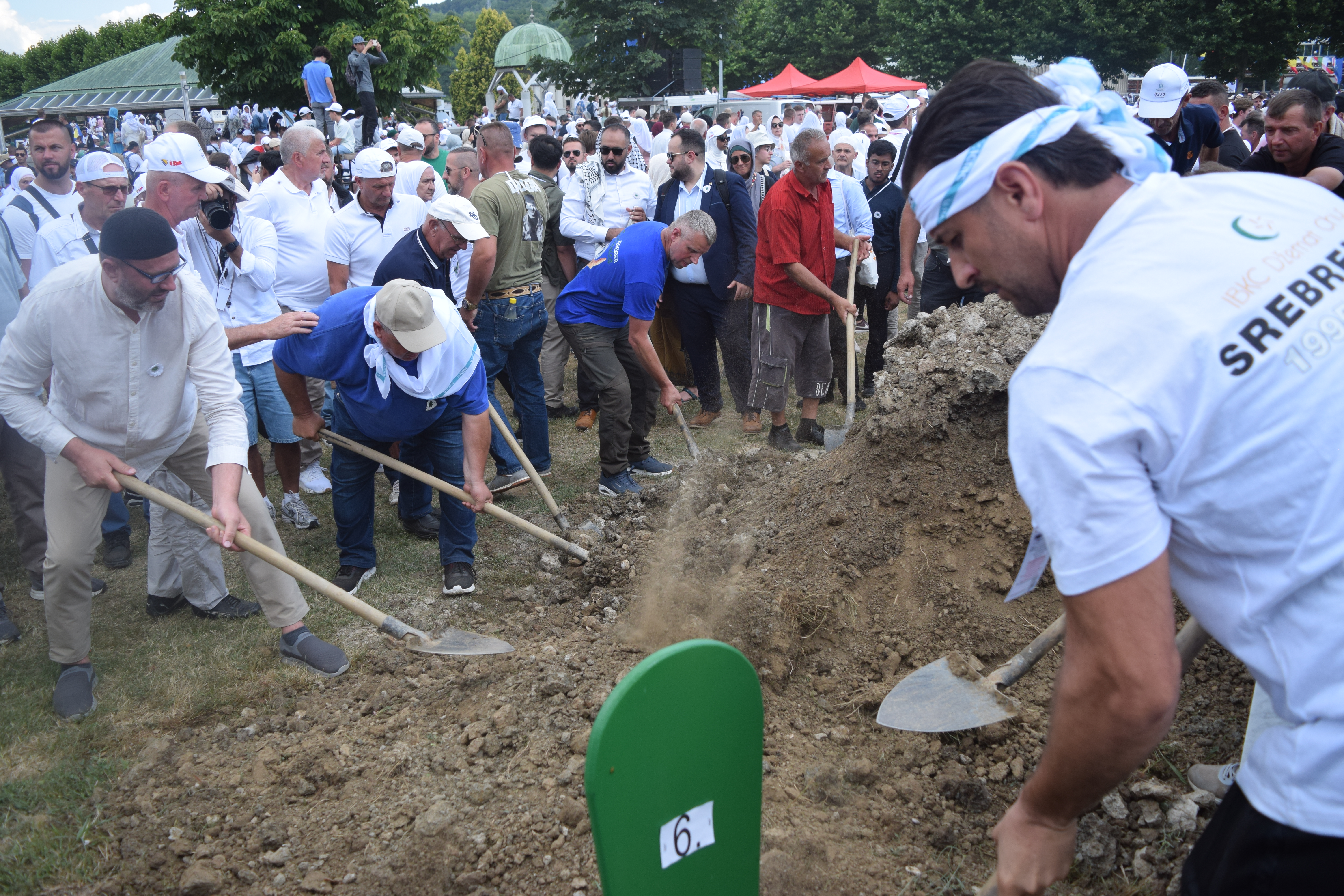 Men take turns covering the caskets with soil, shoveling from nearby mounds of dirt.