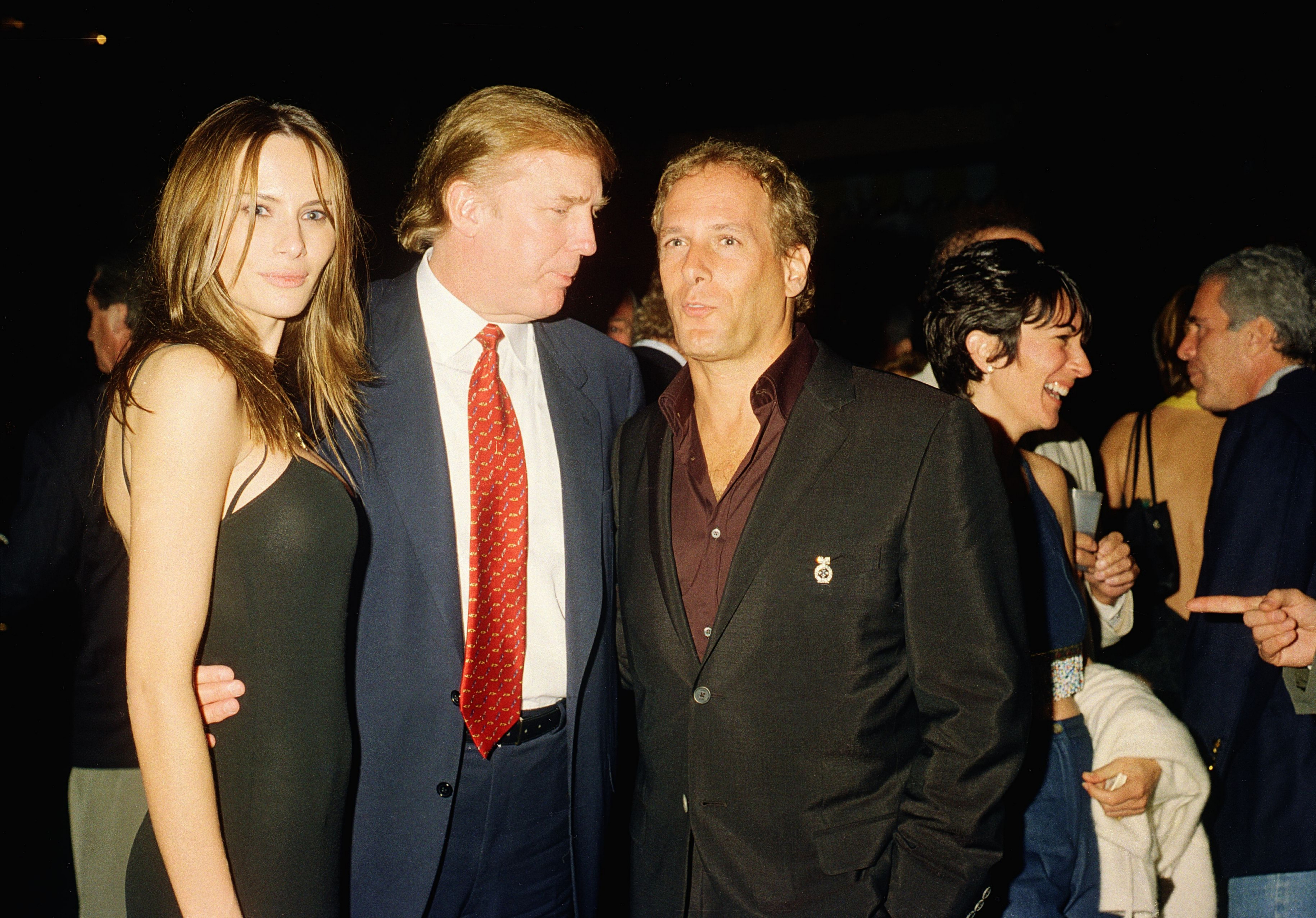View of former model Melania Knauss (later Trump) and her boyfriend (and future husband) real estate developer Donald Trump (center) as they pose with musician Michael Bolton at the Mar-a-Lago club, Palm Beach, Florida, February 12, 2000. Among those visible in the background are British socialite Ghislaine Maxwell (second right) and American financier Jeffrey Epstein (1953 - 2019)