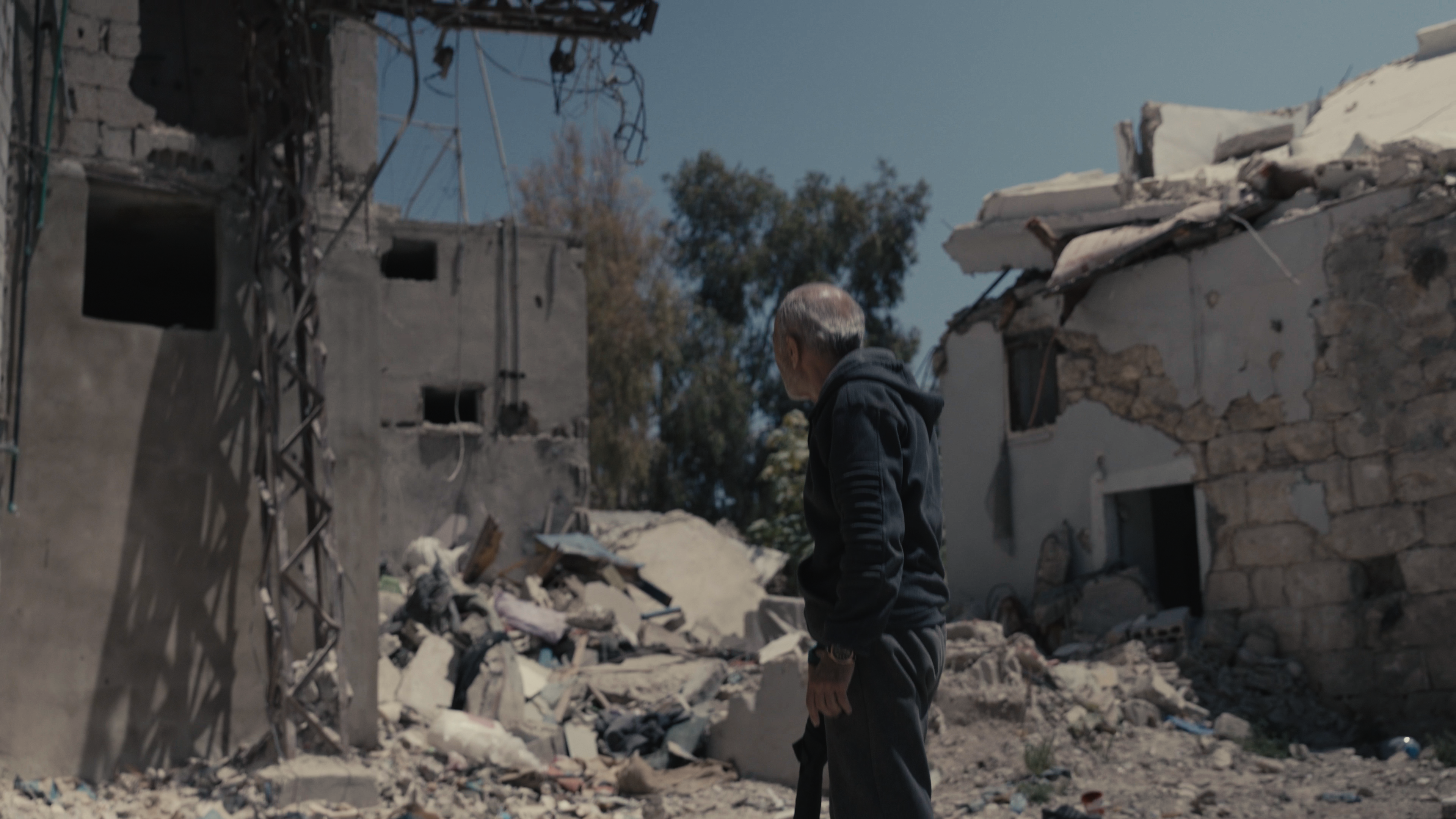 A man stands with his back turned as he looks upon the rubble of a destroyed building