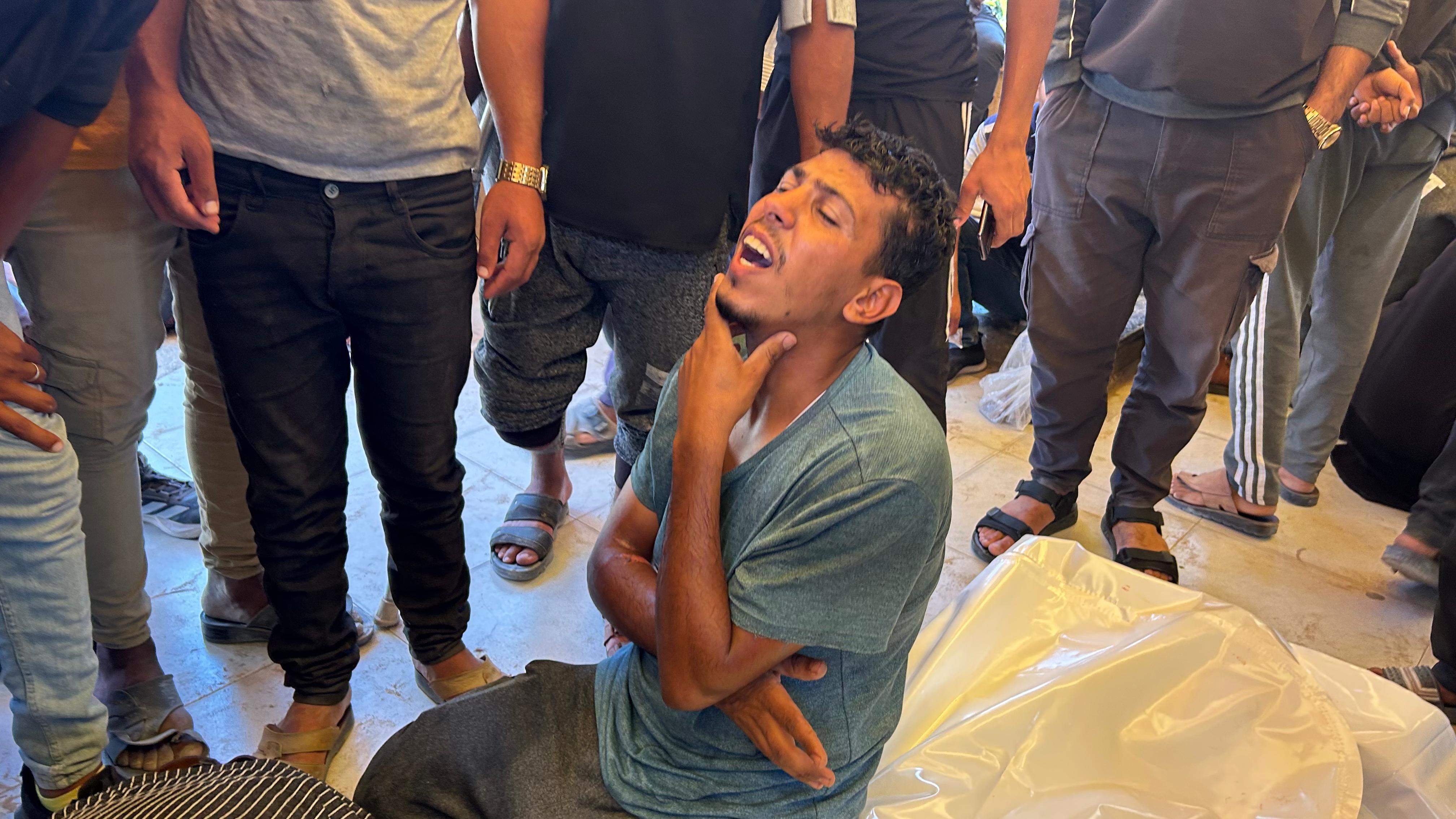 Man expresses emotion as he sits next to a body bag