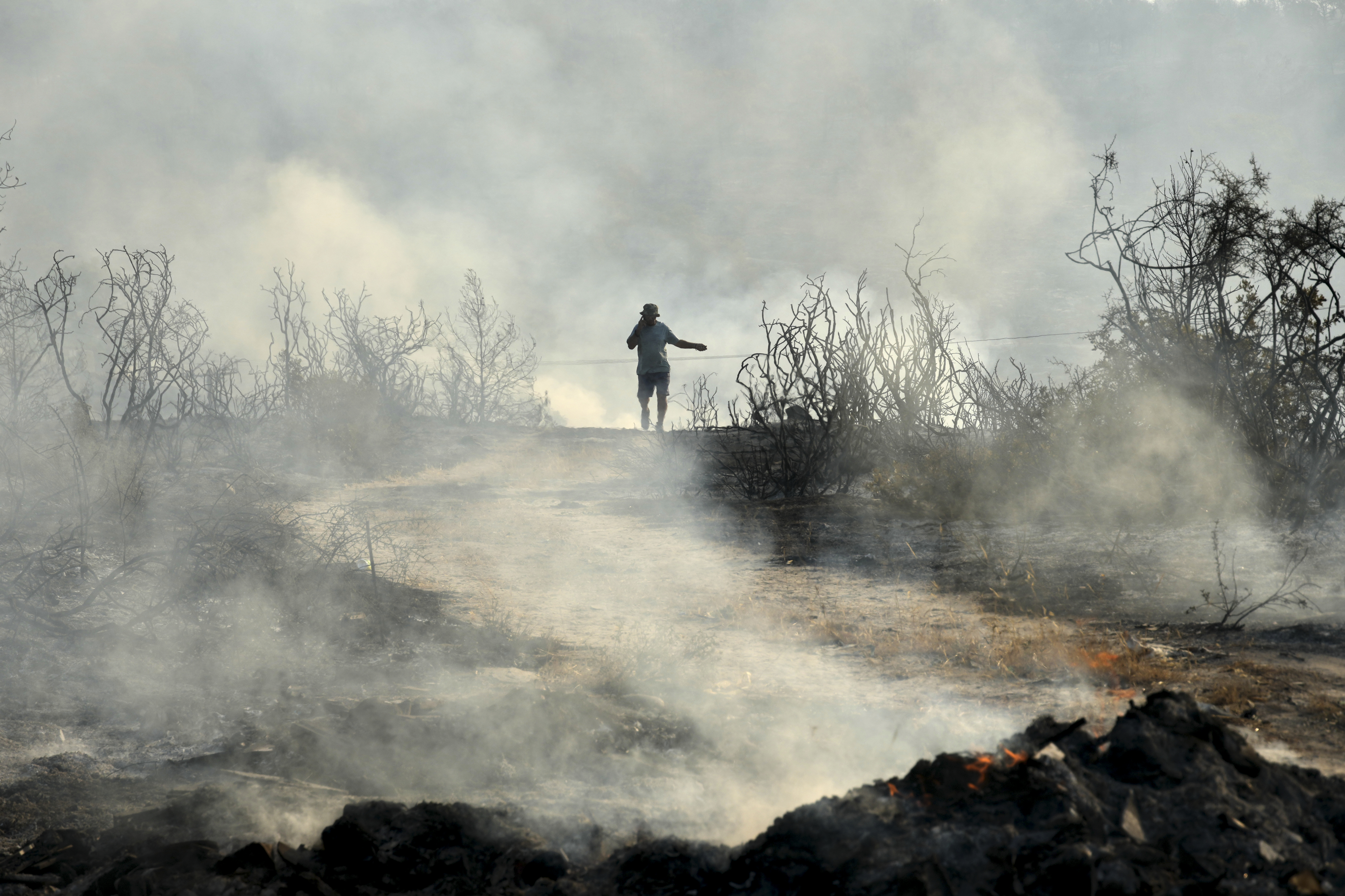 A man speaking on his cellphone walks through a burned area in Souni village, Cyprus, during a massive wildfire on the southern side of the east Mediterranean island nation's Troodos mountain range, Thursday, July 24, 2025. (AP Photo/Petros Karadjias)