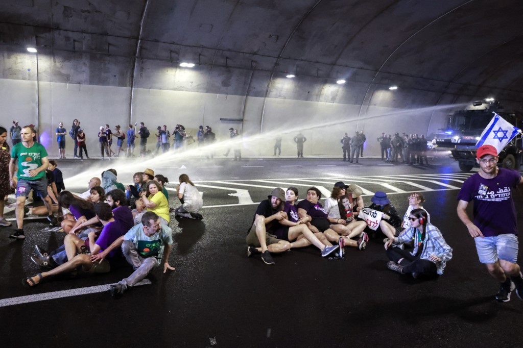 Israeli police use a water cannon to disperse demonstrators blocking traffic in a tunnel. [Menahem Kahana/AFP)