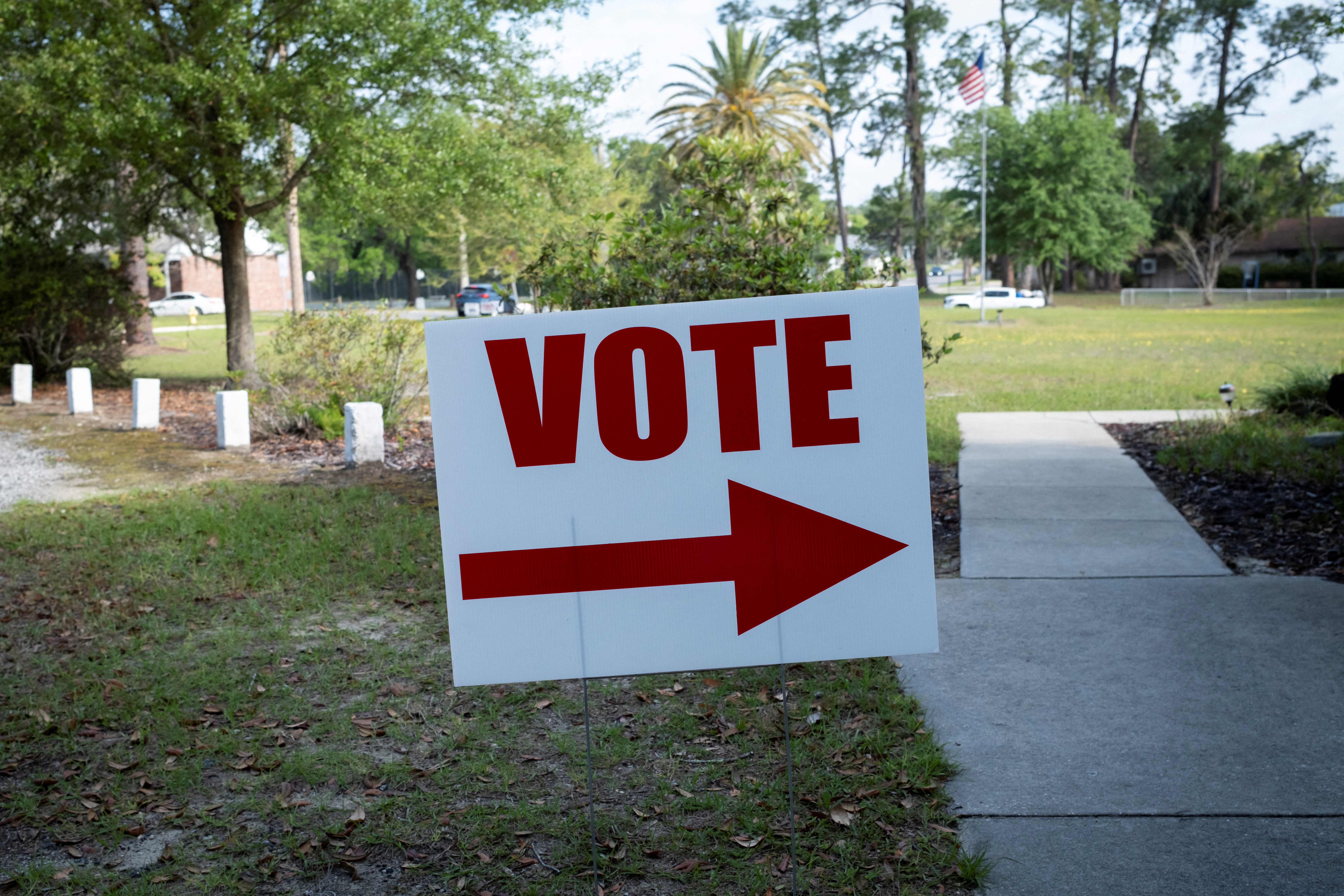 A vote sign sits next to a sidewalk on a grassy area.