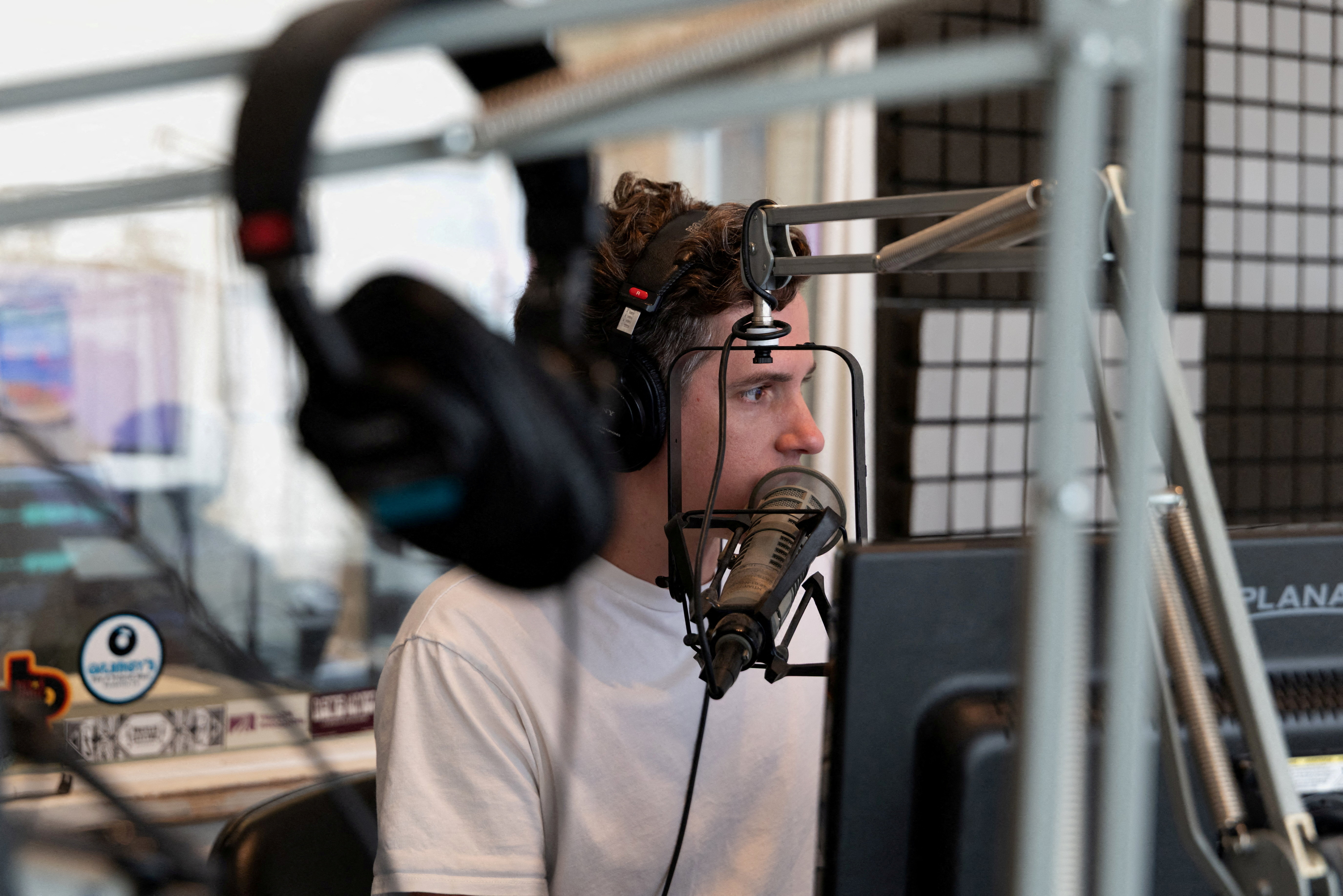 A news broadcaster sits in front of a computer screen with headphones in the foreground.