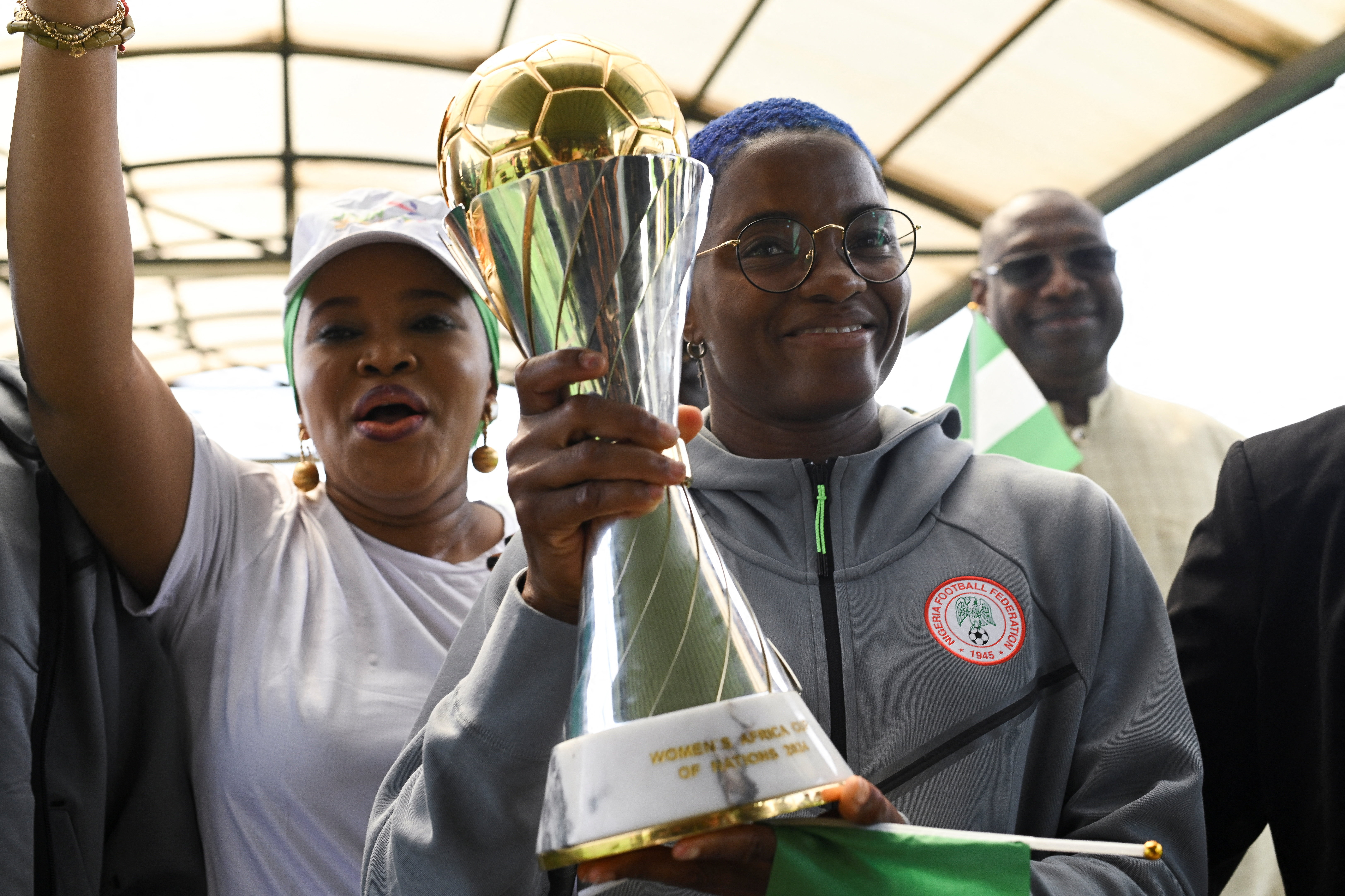 Nigeria’s Super Falcons captain Rasheedat Ajibade holds the 2024 WAFCON trophy as supporters cheer at Nnamdi Azikiwe International Airport in Abuja
