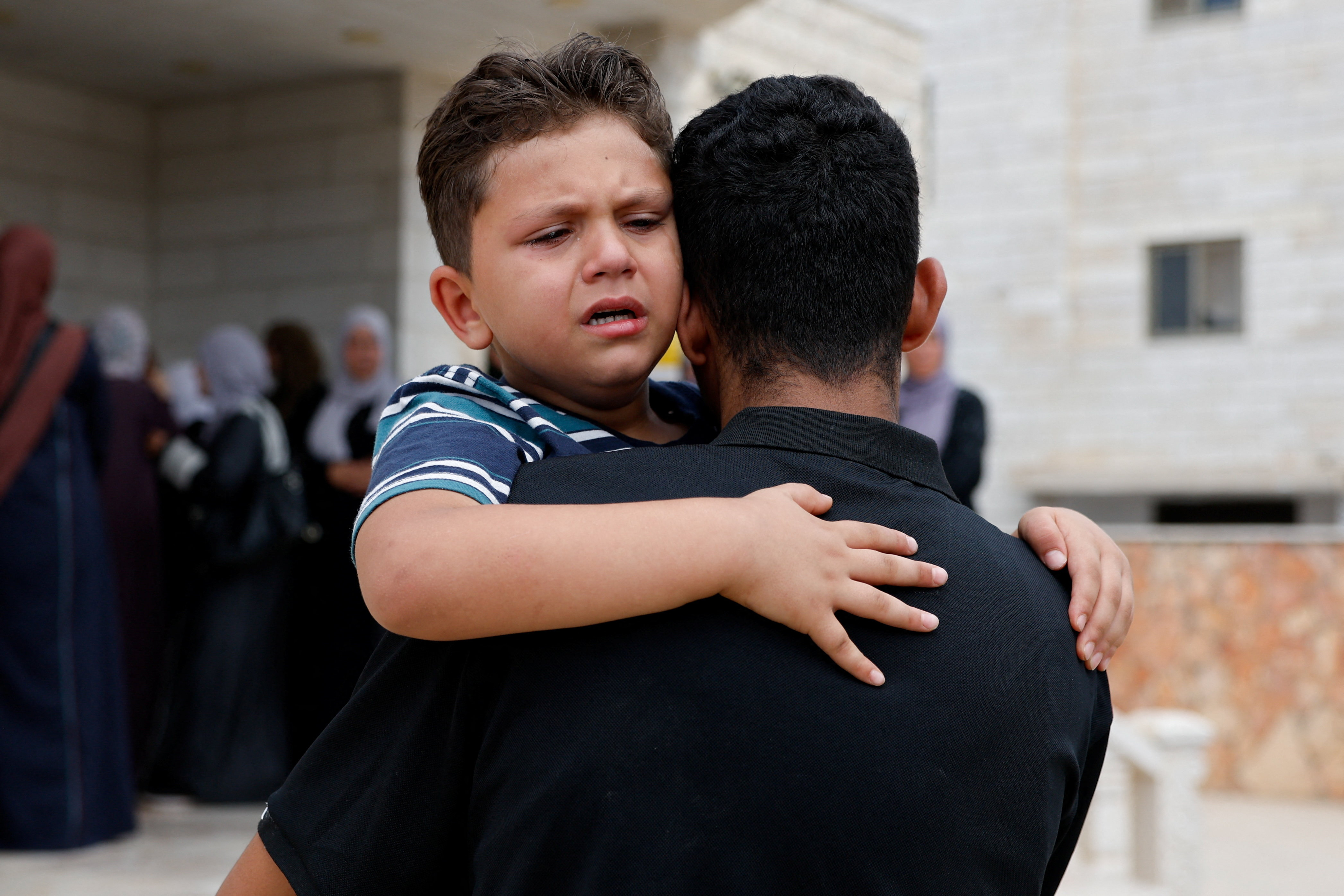Judeh, Khamis Ayyad's son, hugs a family member who carries him in a bear hug.