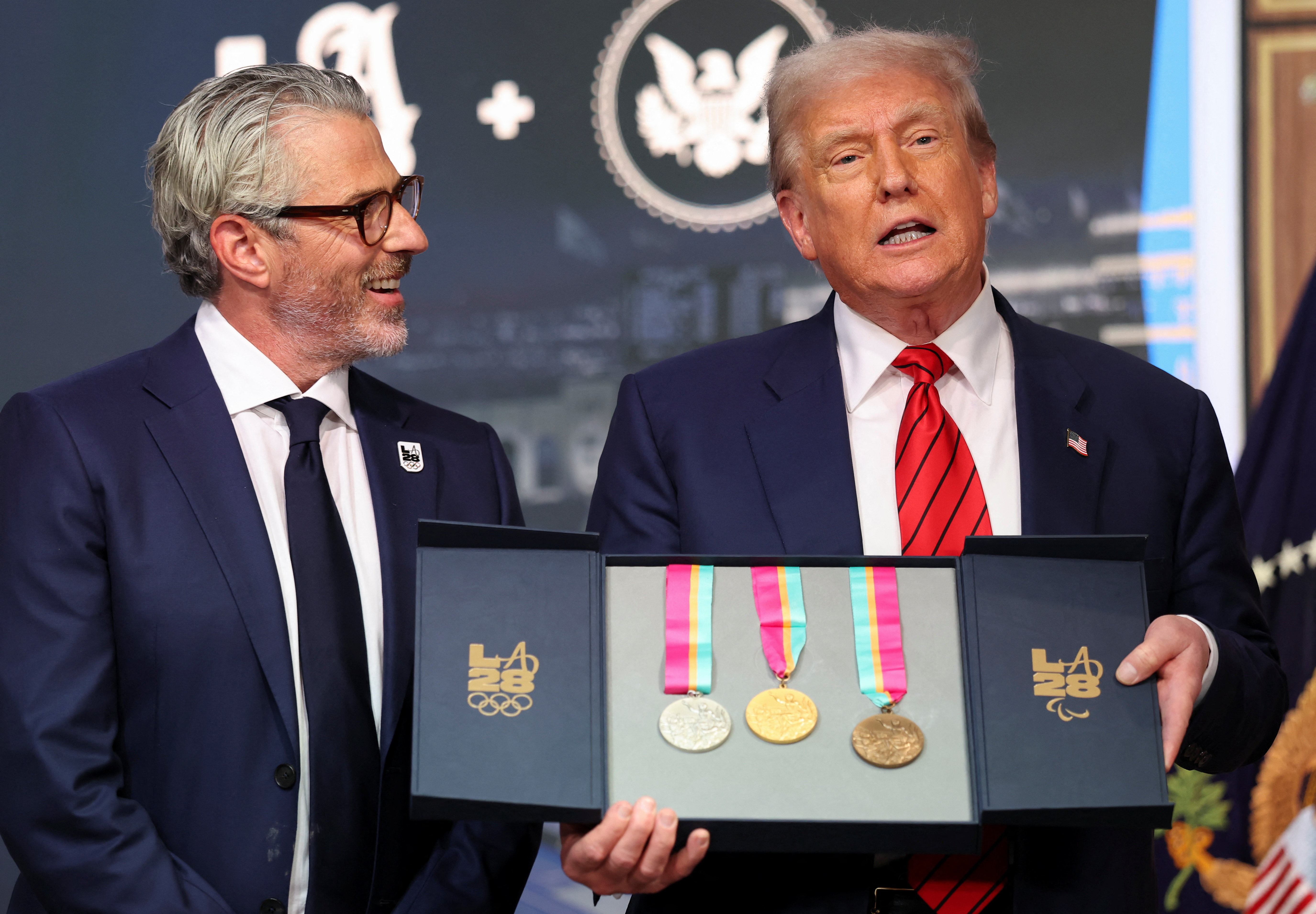 U.S. President Donald Trump, accompanied by LA28 Chairman Casey Wasserman, holds 1984 Los Angeles Olympics medals as he delivers remarks before signing an executive order to create a White House Olympics task force to handle security and other issues related to the 2028 summer Olympic games