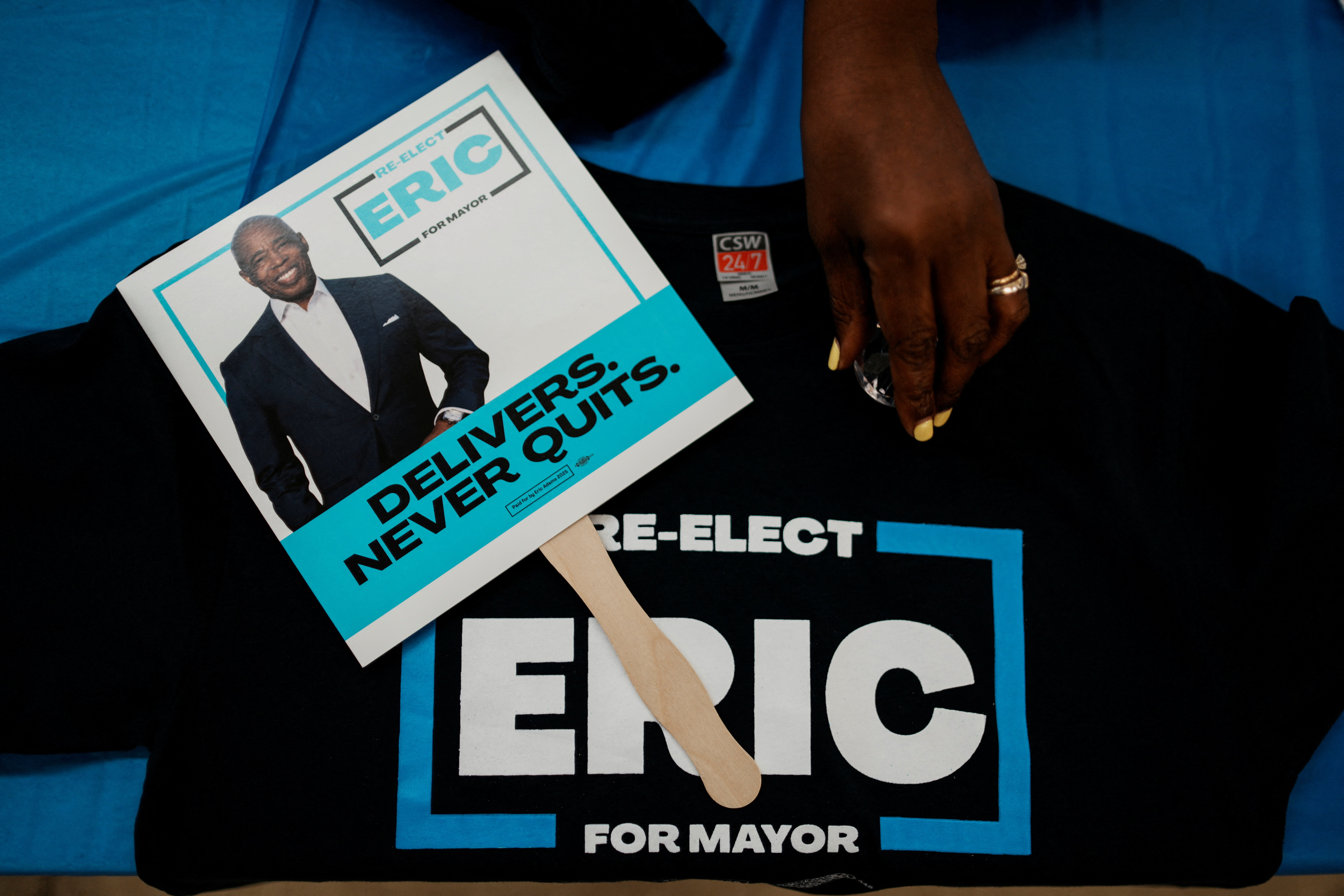 A supporter for Eric Adams peruses a sign of support displayed against an Adams-themed T-shirt on a table.