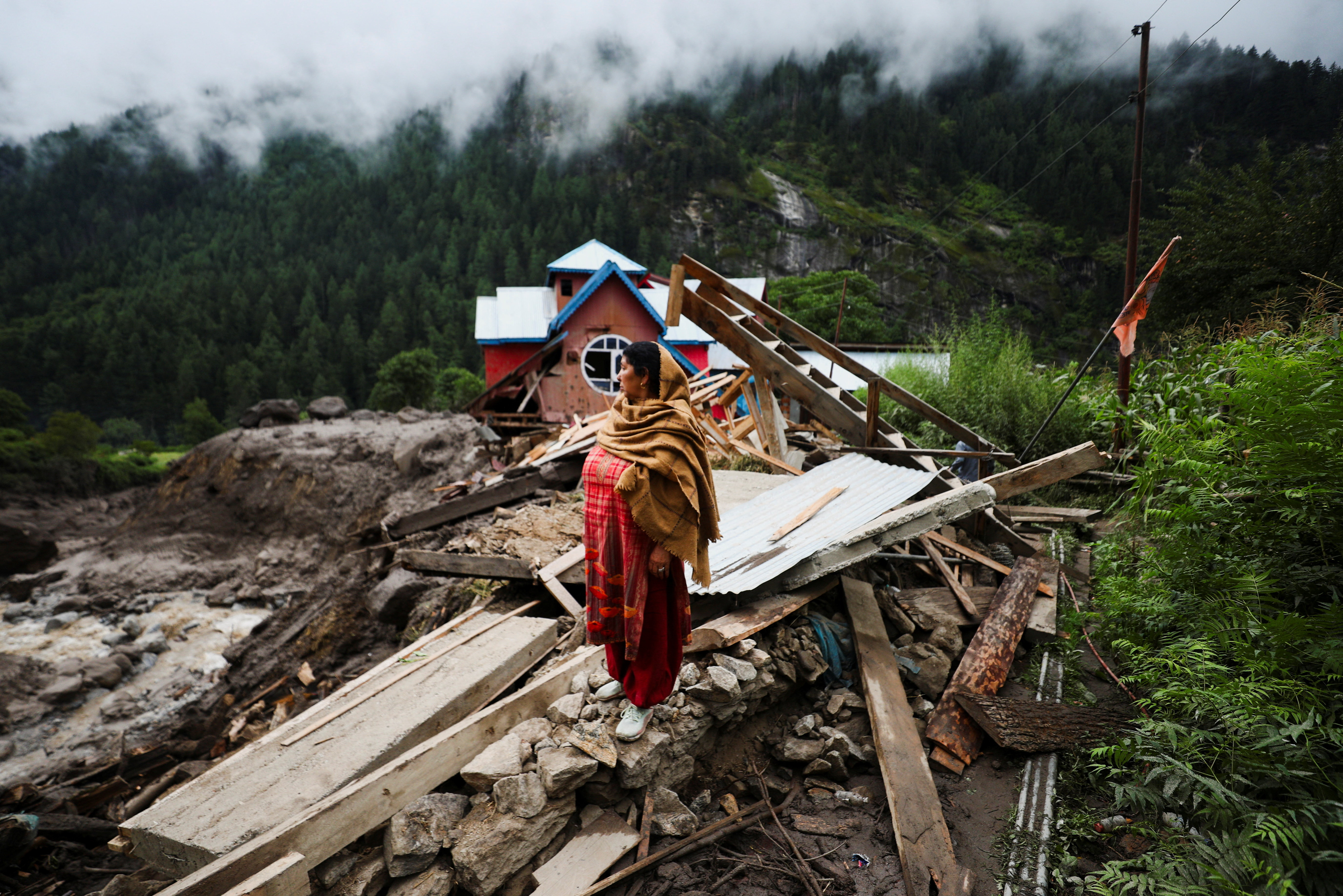 A woman stands in front of houses damaged by the deadly flood caused by sudden, heavy rain in Chasoti town of Kishtwar district, Indian Kashmir, August 15, 2025. REUTERS/Stringer REFILE - QUALITY REPEAT