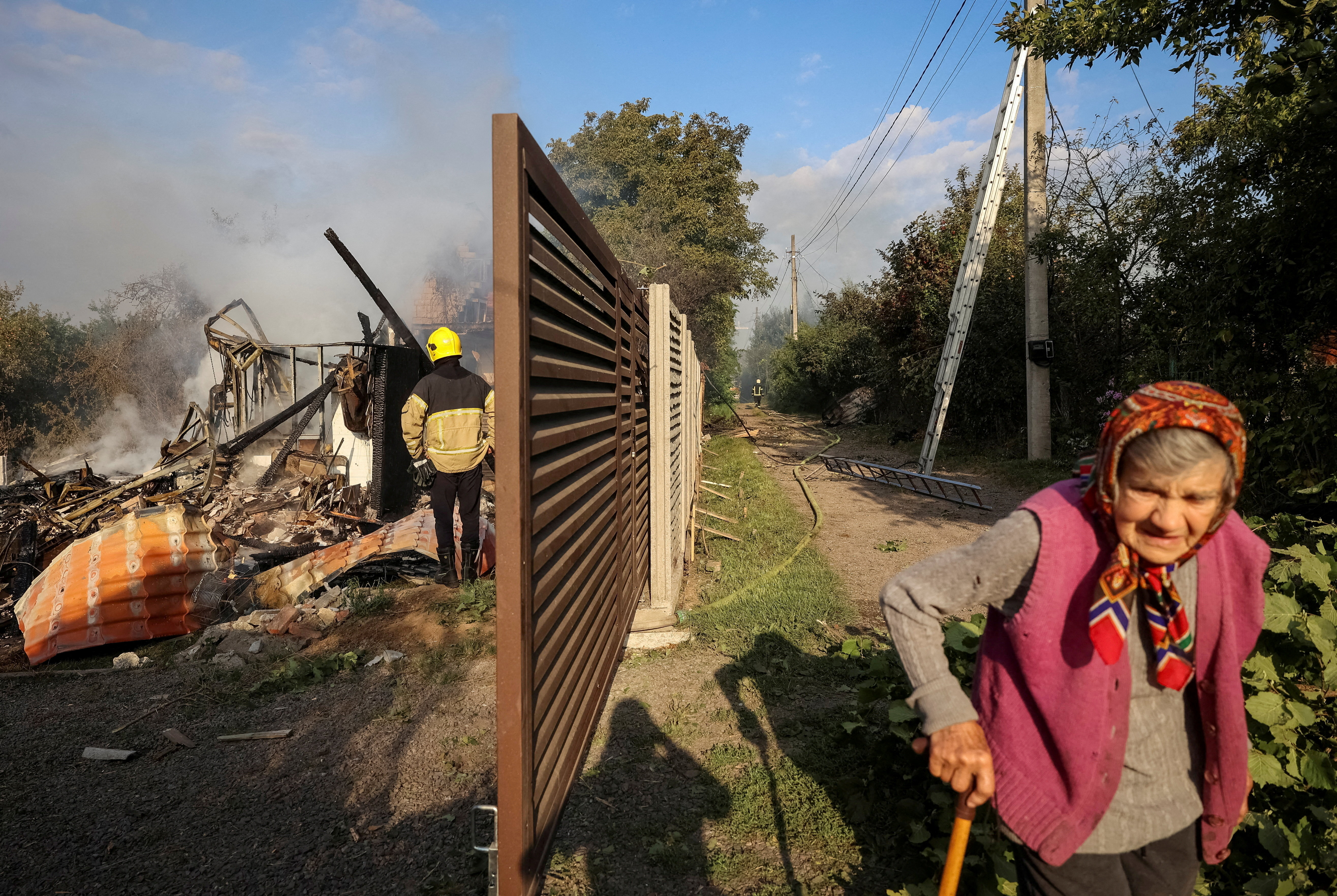 A resident walks along a street as a firefighter works at the site of a Russian missile strike, amid Russia's attack on Ukraine, in the village of Sknyliv on the outskirts of Lviv, Ukraine August 21, 2025. REUTERS/Roman Baluk TPX IMAGES OF THE DAY