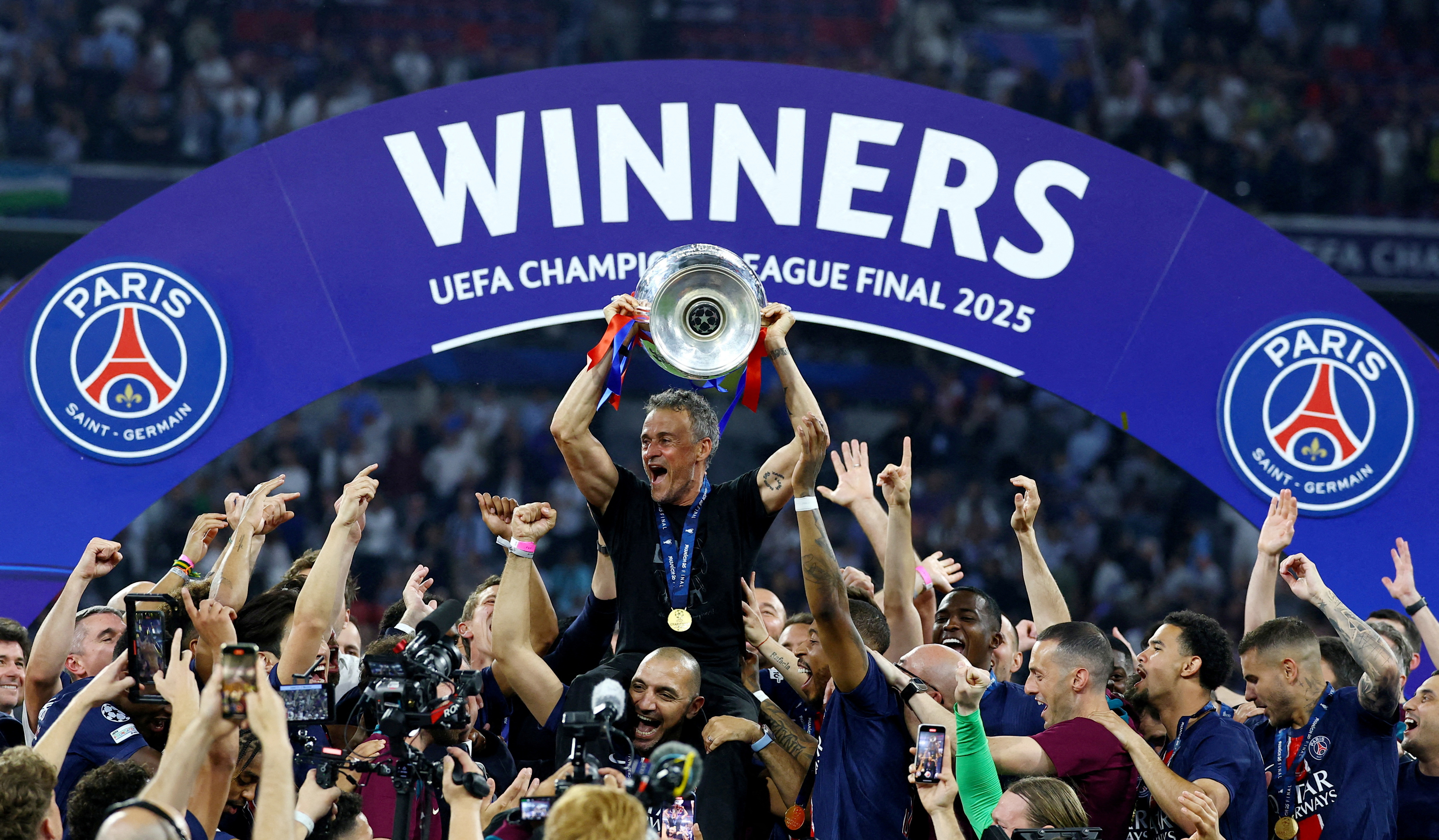 Paris Saint-Germain coach Luis Enrique lifts the trophy as he celebrates with his players after winning the Champions League