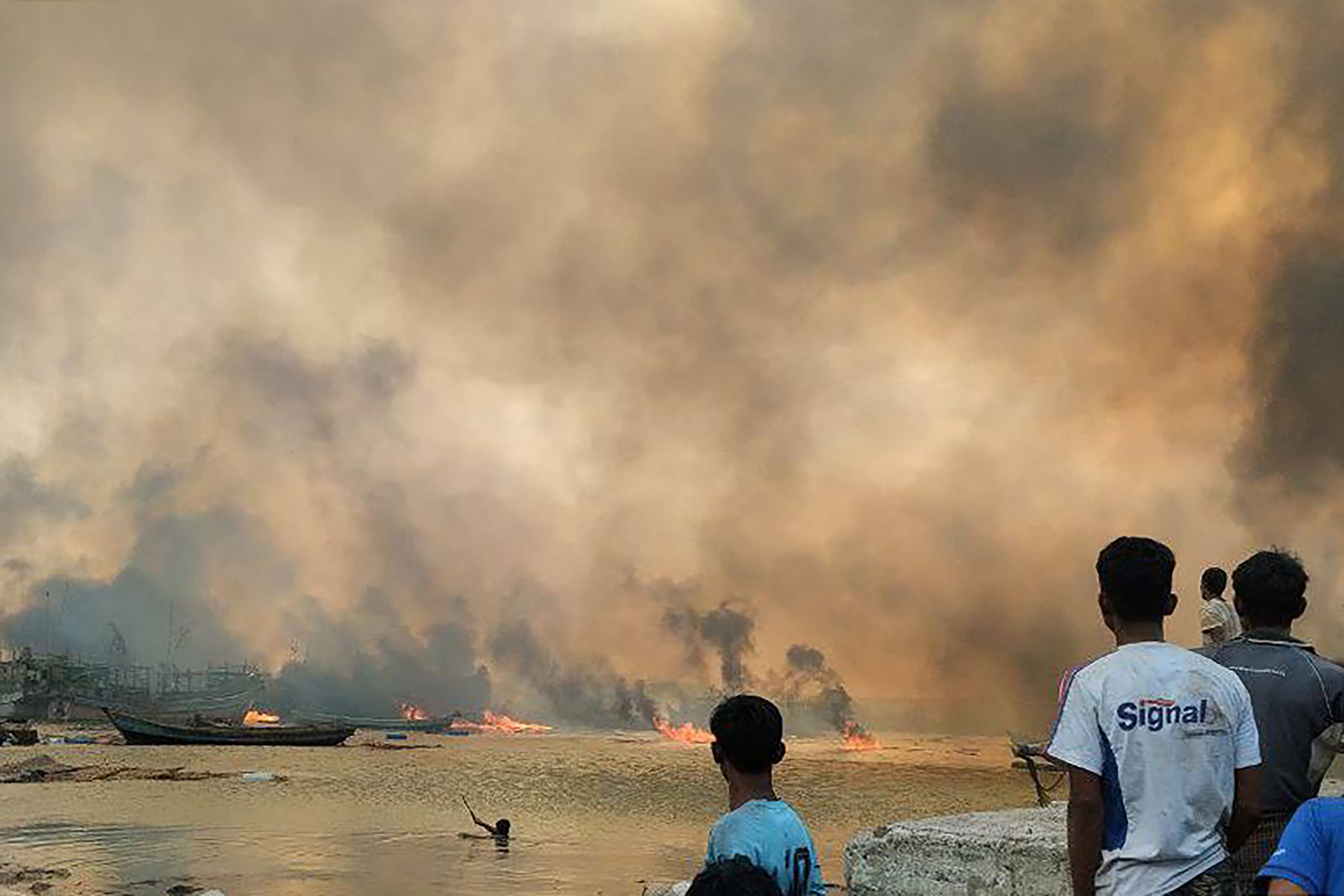 This handout photo taken and released on January 9, 2025 by the Arakan Army (AA) ethnic minority armed group shows people looking at burning homes at the site of a suspected air strike carried out by Myanmar's military at Kyauk Ni Maw village in Ramree island in western Rakhine State. A Myanmar junta air strike killed at least 40 people in a town in western Rakhine state, a rescue worker and ethnic minority armed group told AFP on January 9, 2025. (Photo by Handout / Arakan Army (AA) / AFP) / -----EDITORS NOTE --- RESTRICTED TO EDITORIAL USE - MANDATORY CREDIT "AFP PHOTO / ARAKAN ARMY (AA) " - NO MARKETING - NO ADVERTISING CAMPAIGNS - DISTRIBUTED AS A SERVICE TO CLIENTS