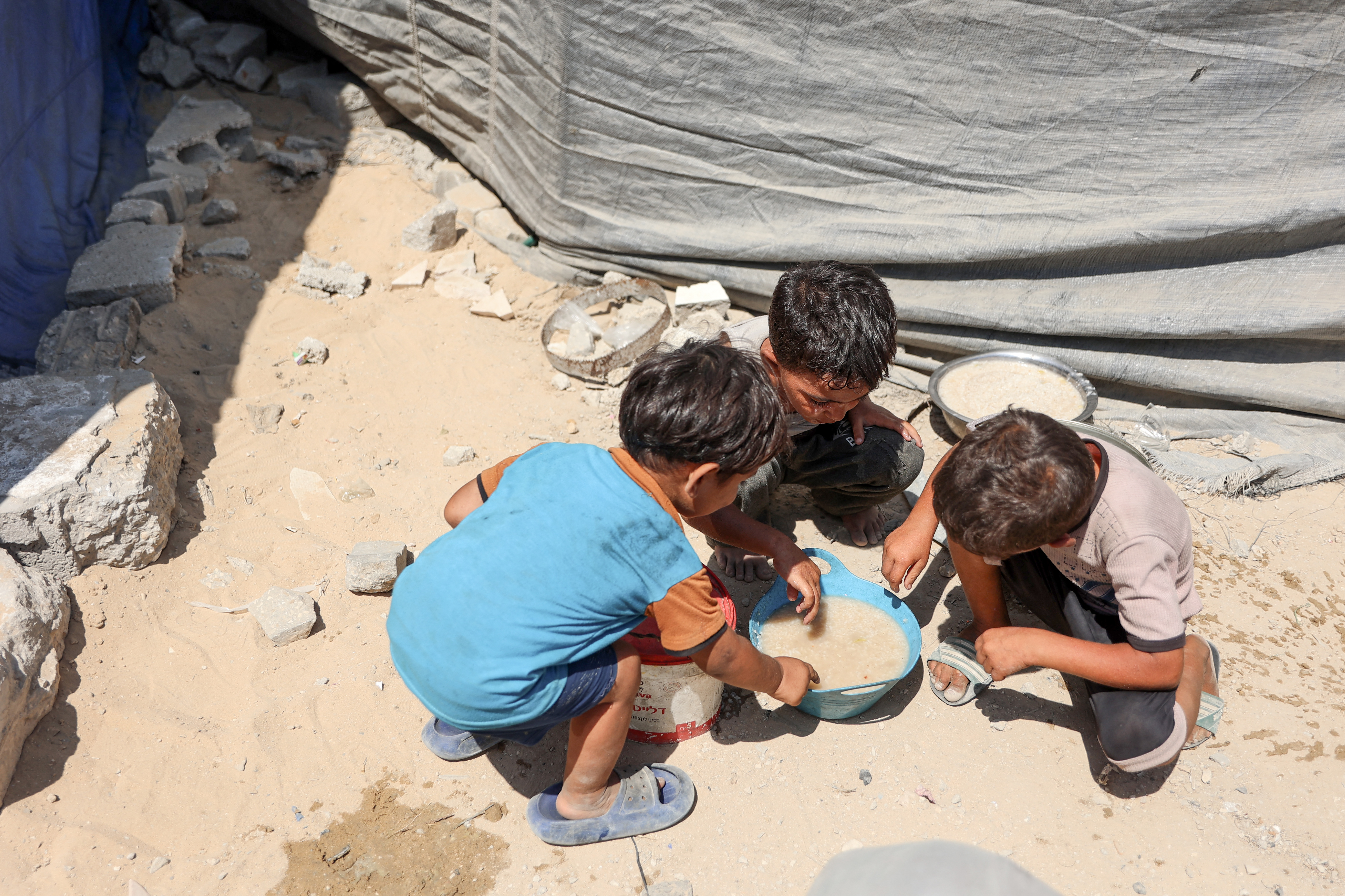 Palestinian children share a bowl of lentil soup obtained from a food distribution point.