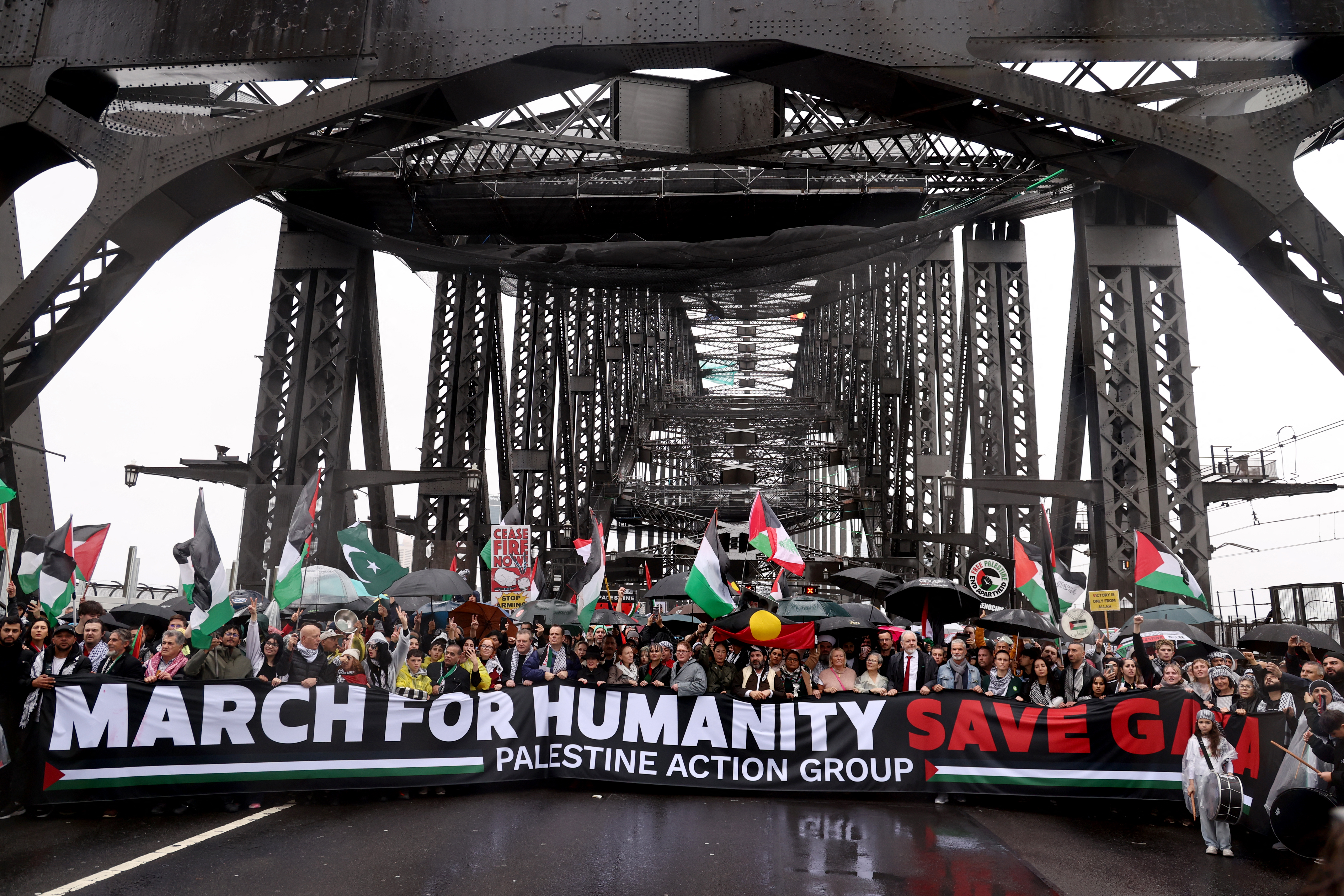 people march behind a banner that says march for humanity save gaza on a bridge