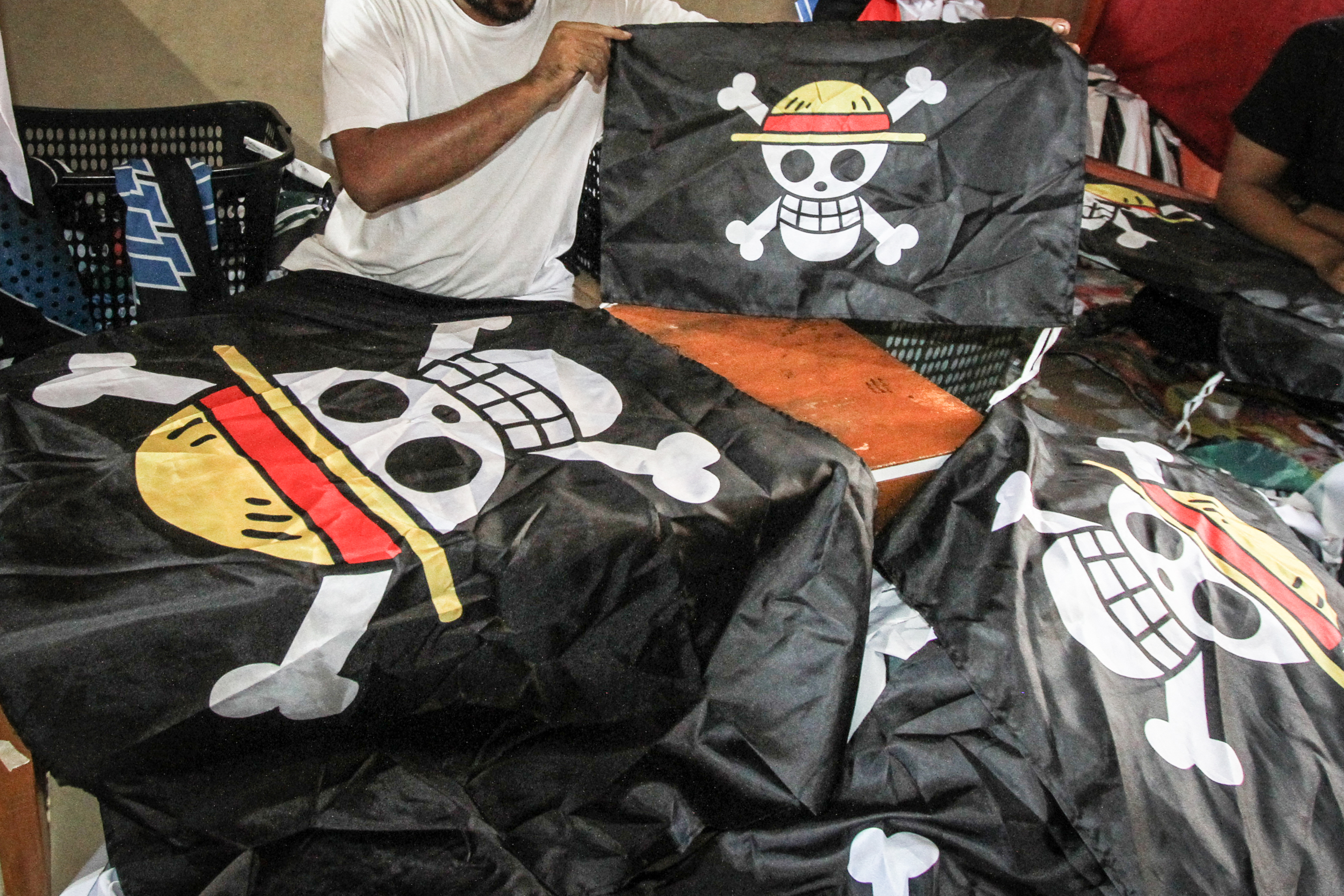 A worker holds a replica of the pirate flag from Japanese anime One Piece, made for sale as some Indonesians adopt the symbol from a story about resisting a corrupt world government to express frustration with their own, at a T-shirt workshop in Karanganyar, Central Java, on August 6, 2025, ahead of the countrys 80th Independence Day. As Indonesia's independence day approaches red and white flags will be flown across the country, but a viral anime pirate banner has drawn government threats against flying the swashbuckling ensign. A Jolly Roger skull and bone symbol topped with a straw hat from Japan's anime series 'One Piece' has caused concern among officials in Jakarta that it is being used to criticise President Prabowo Subianto's policies. (Photo by DIKA / AFP) / TO GO WITH 'INDONESIA-POLITICS-PROTEST-ANIME, FOCUS' BY DESSY SAGITA & JACK MOORE