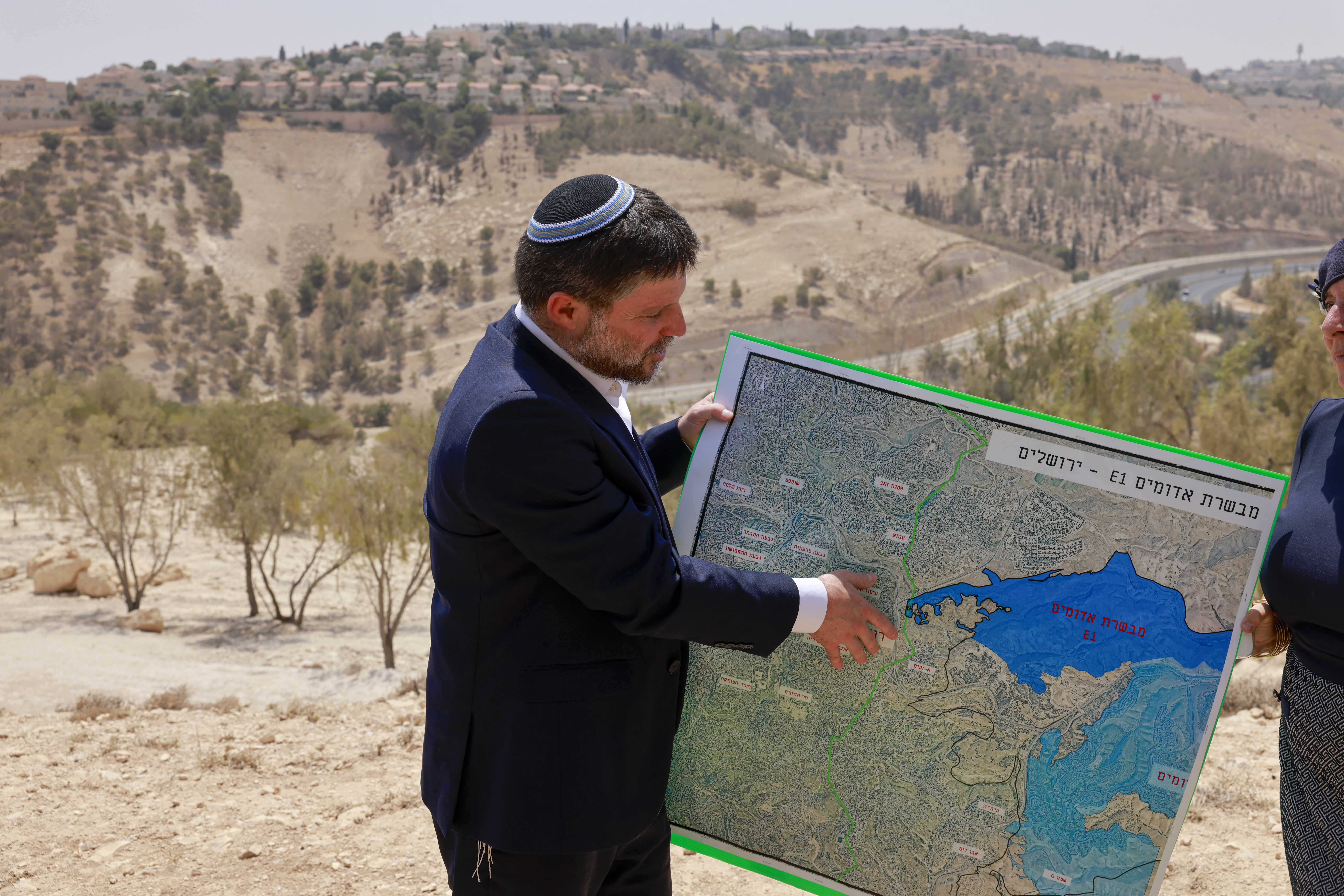 Israeli far-right Finance Minister Bezalel Smotrich holds a map of an area near the settlement of Maale Adumim, a land corridor known as E1, outside Jerusalem in the occupied West Bank, on August 14, 2025, after a press conference at the site. [Menahem Kahana/AFP]