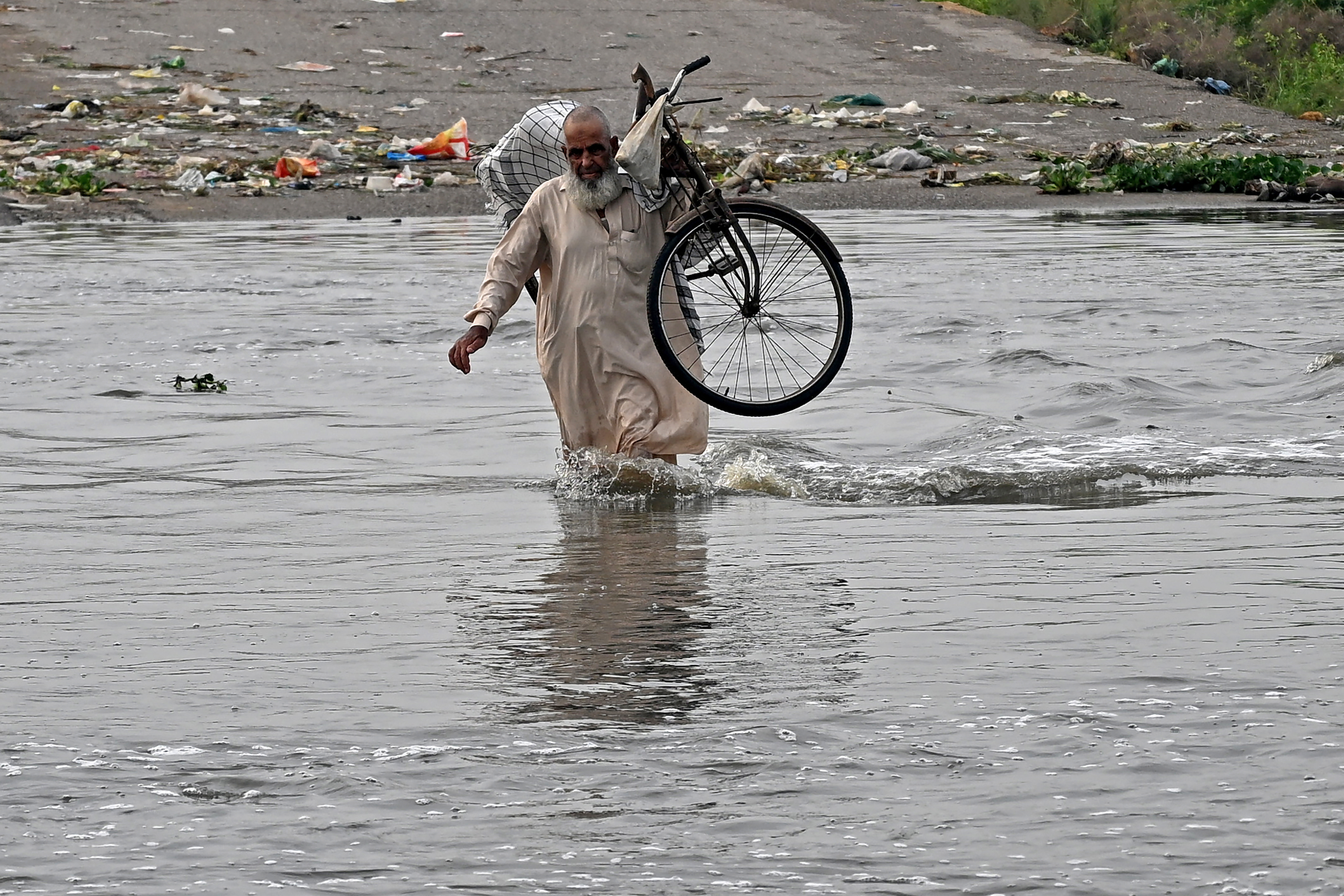 A man carries his bicycle as he wades along a flooded road after heavy monsoon rains in Karachi on August 20
