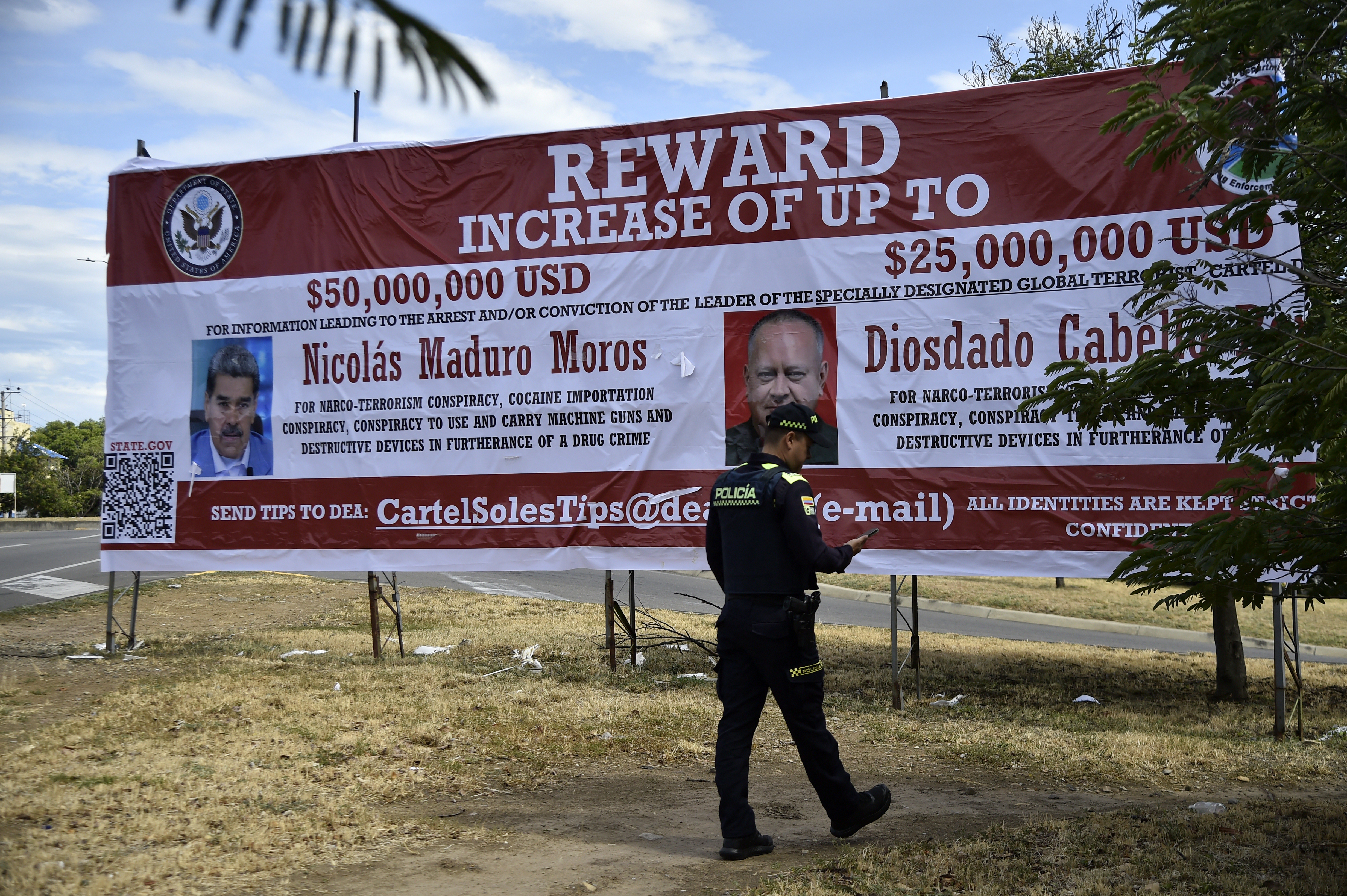 A Colombian police officer walks in front of a banner offering a reward for information leading to the arrest of Venezuelan President Nicolas Maduro and Venezuela's Minister of Interior Relations, Justice, and Peace, Diosdado Cabello, in Villa del Rosario, Norte de Santander Department, Colombia, on August 23, 2025. The United States doubled its bounty on Venezuelan President Nicolas Maduro -- who faces federal drug trafficking charges -- to $50 million on August 7, 2025, a move Caracas described as "pathetic" and "ridiculous". (Photo by Schneyder MENDOZA / AFP)