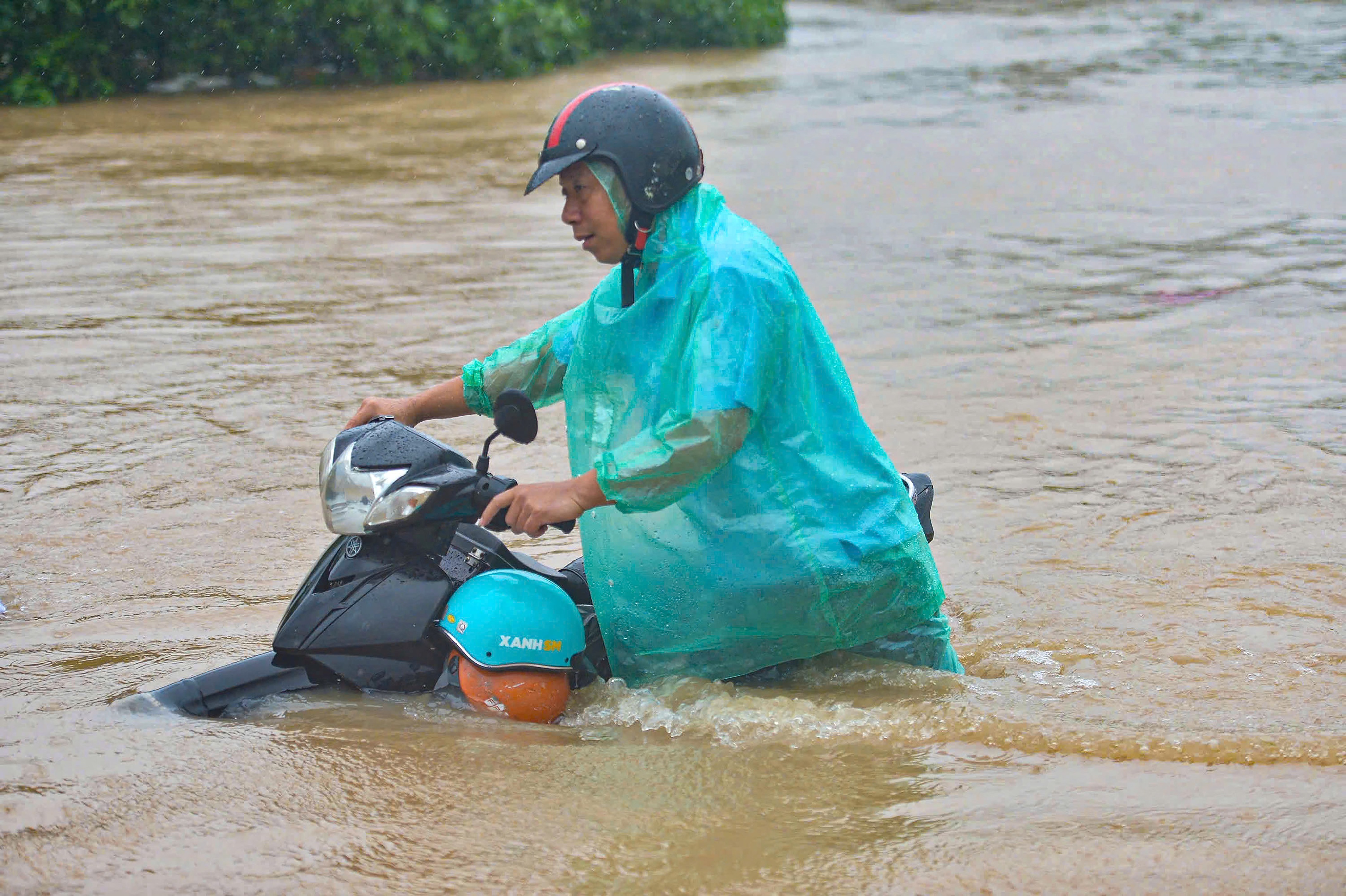 A man pushes a motorbike through a flooded street.