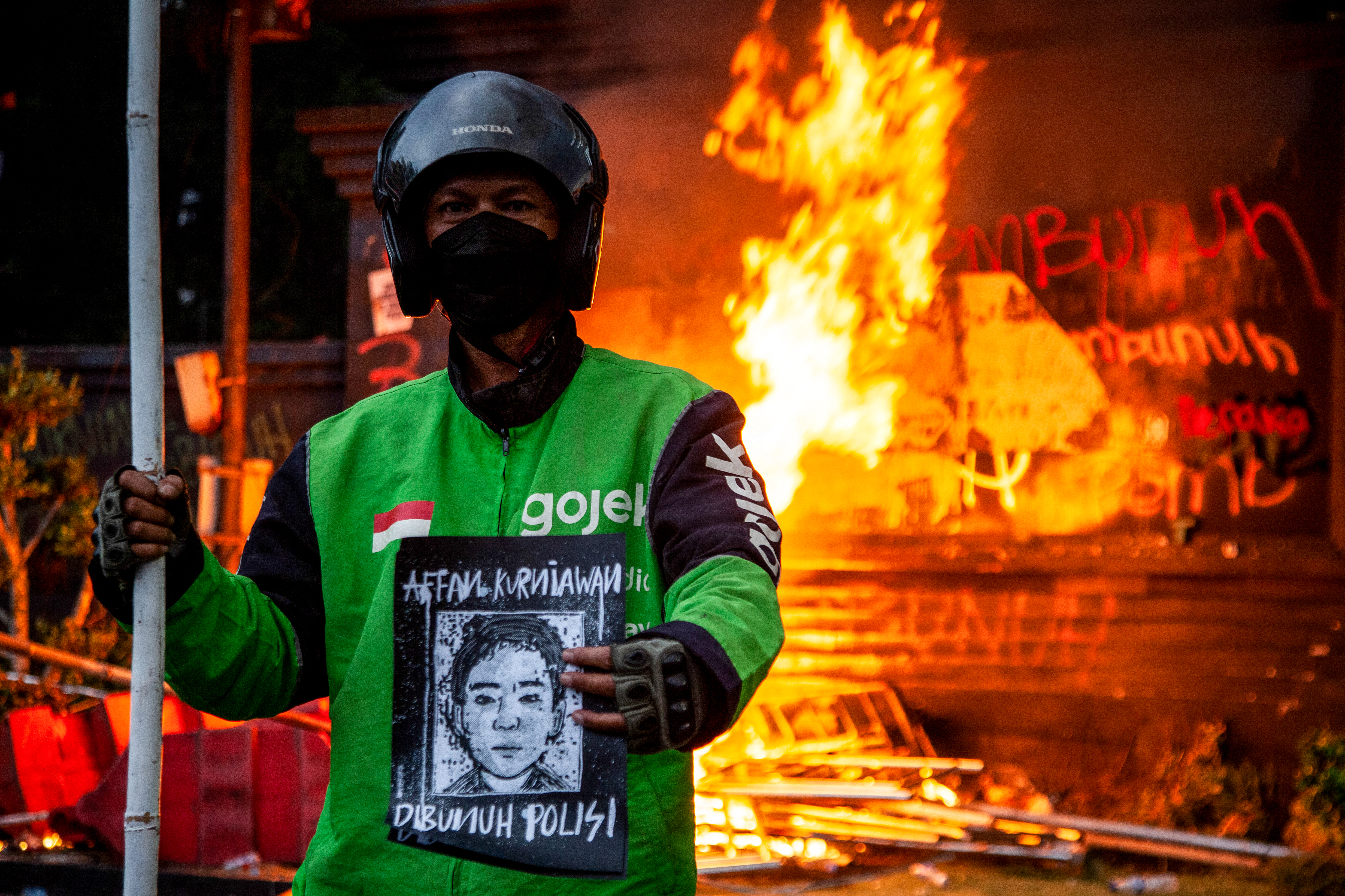 A man wearing a biker's jacket holds a portrait of the motorcycle taxi driver