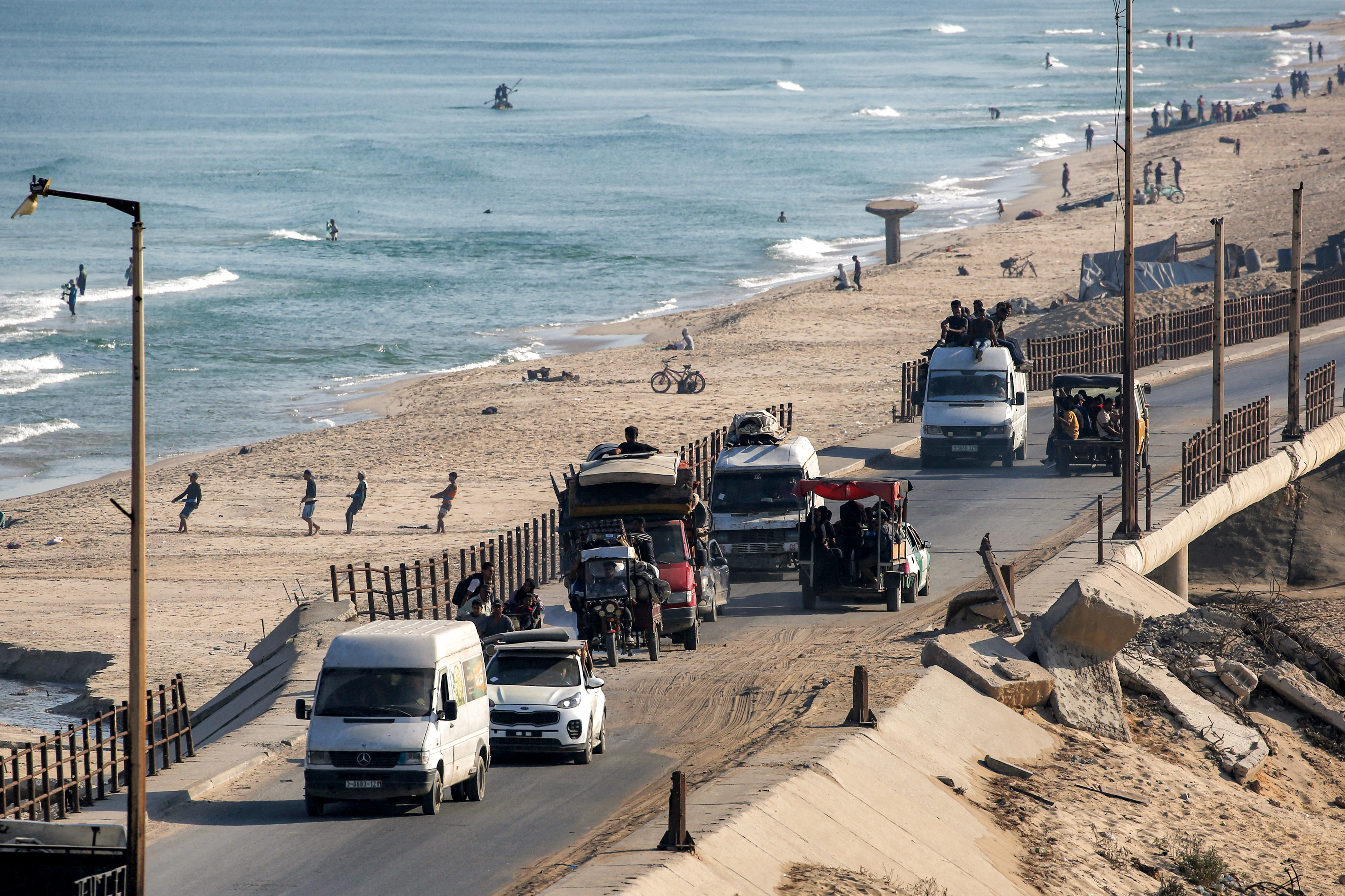 Trucks and vehicles move along the coastal road near fishermen pulling their nets to retrieve their catch on a beach in the Nuseirat camp for Palestinian refugees in the central Gaza Strip