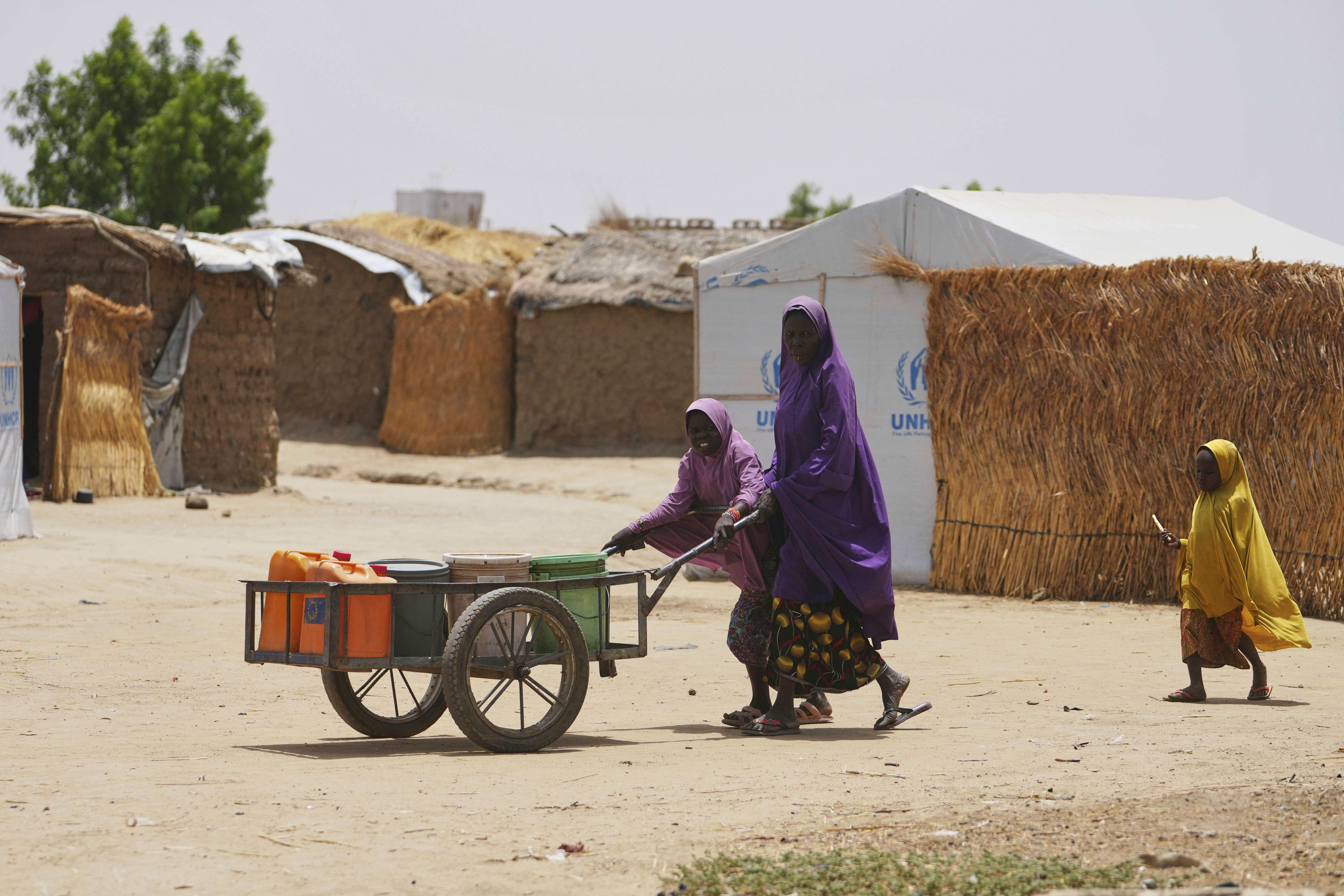 A Displaced woman and two girls push a wheel barrow with jerrycans in Dikwa, Borno