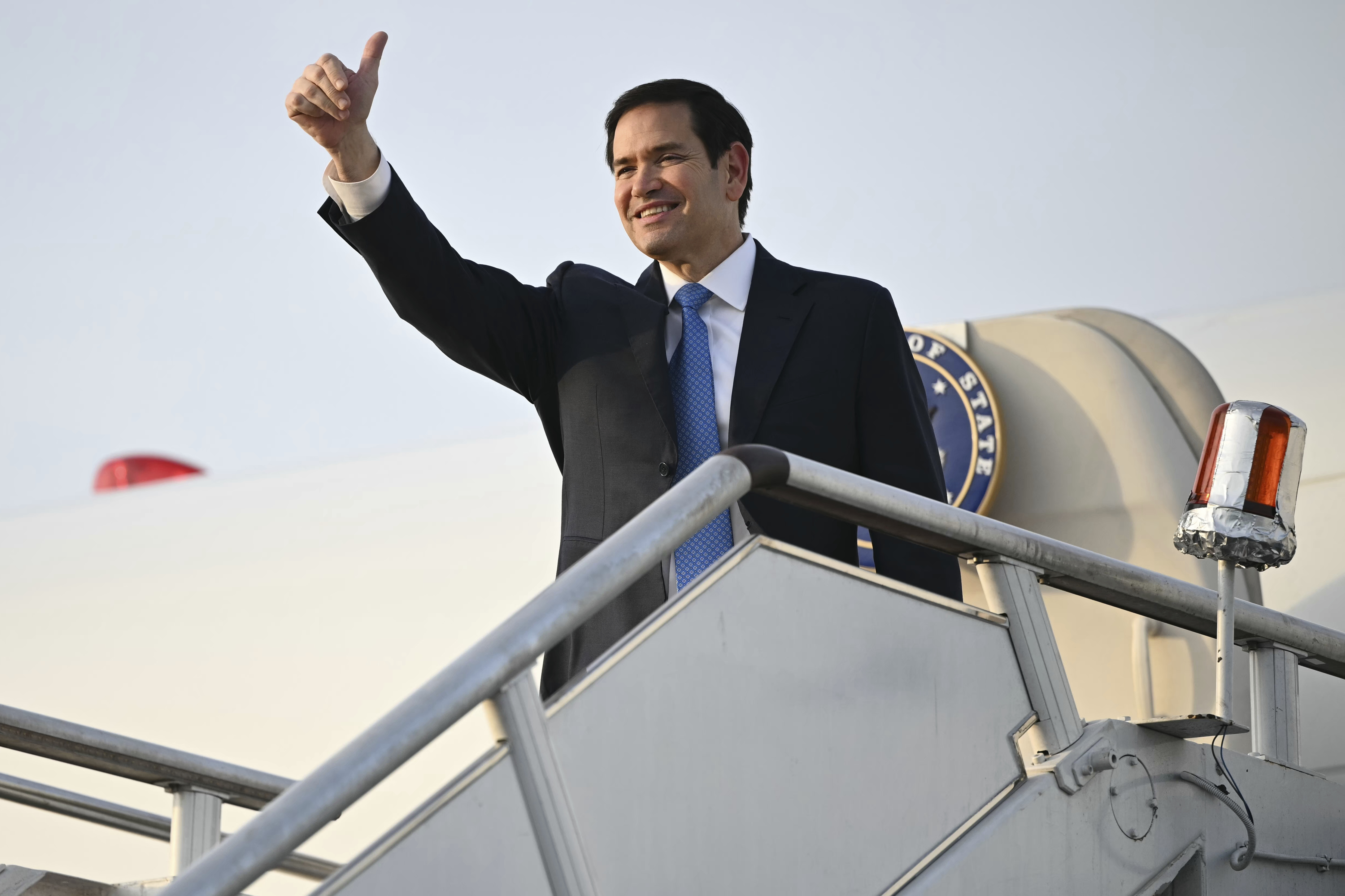 Marco Rubio waves from the staircase to a plane.
