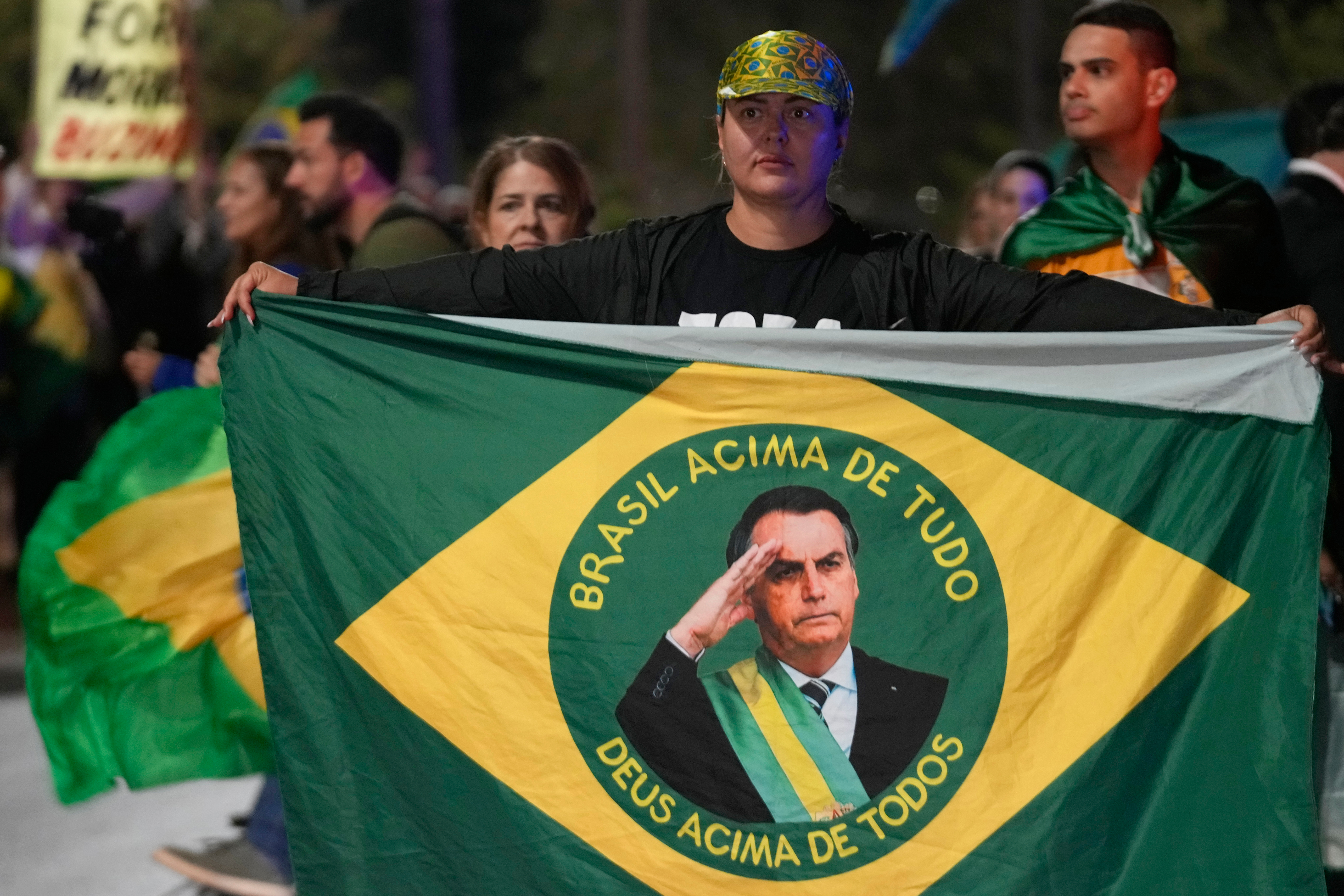 Protesters hold up a Brazilian flag with Bolsonaro's face in the middle.
