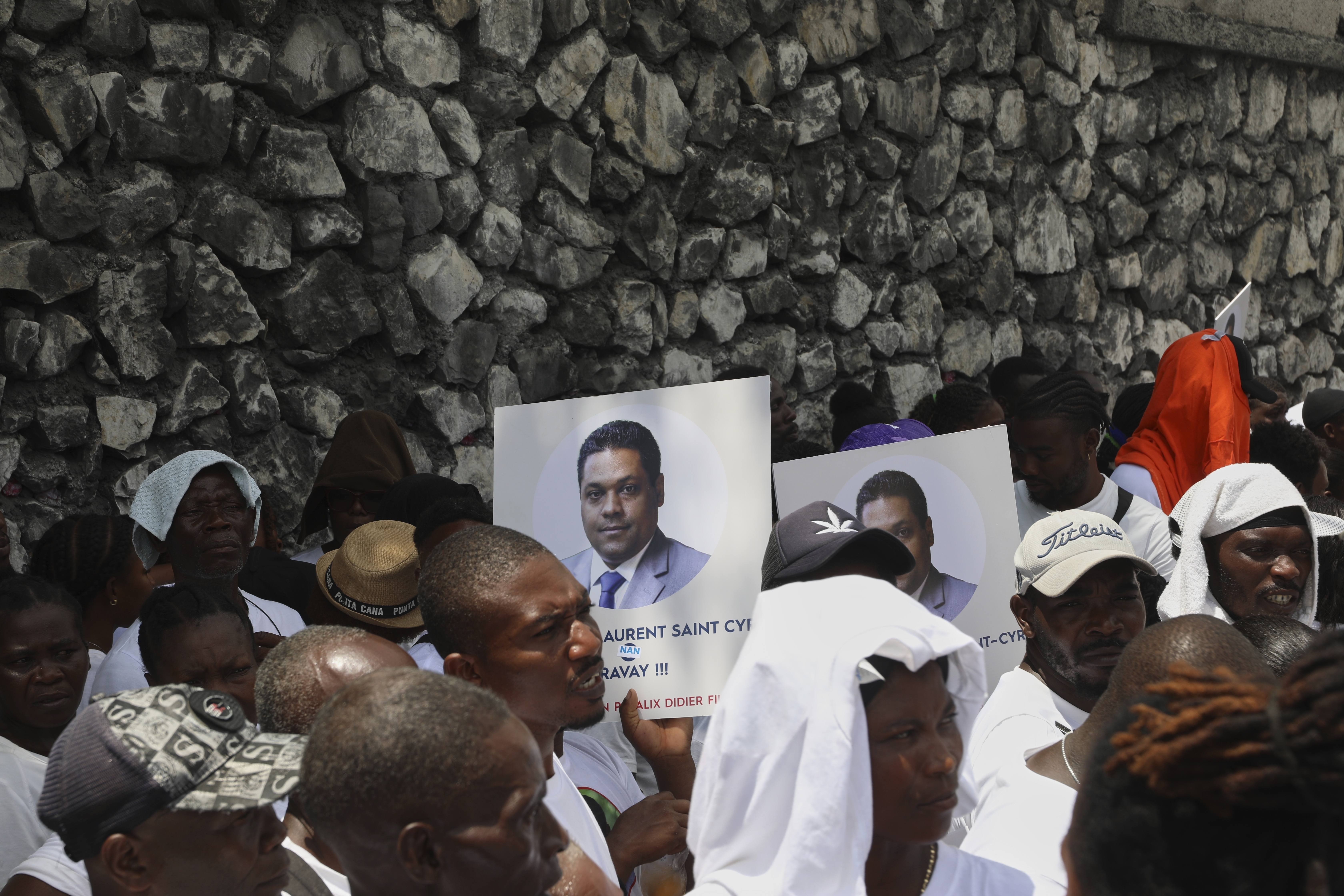 Supporters hold up portraits of Laurent Saint-Cyr outside a stone wall