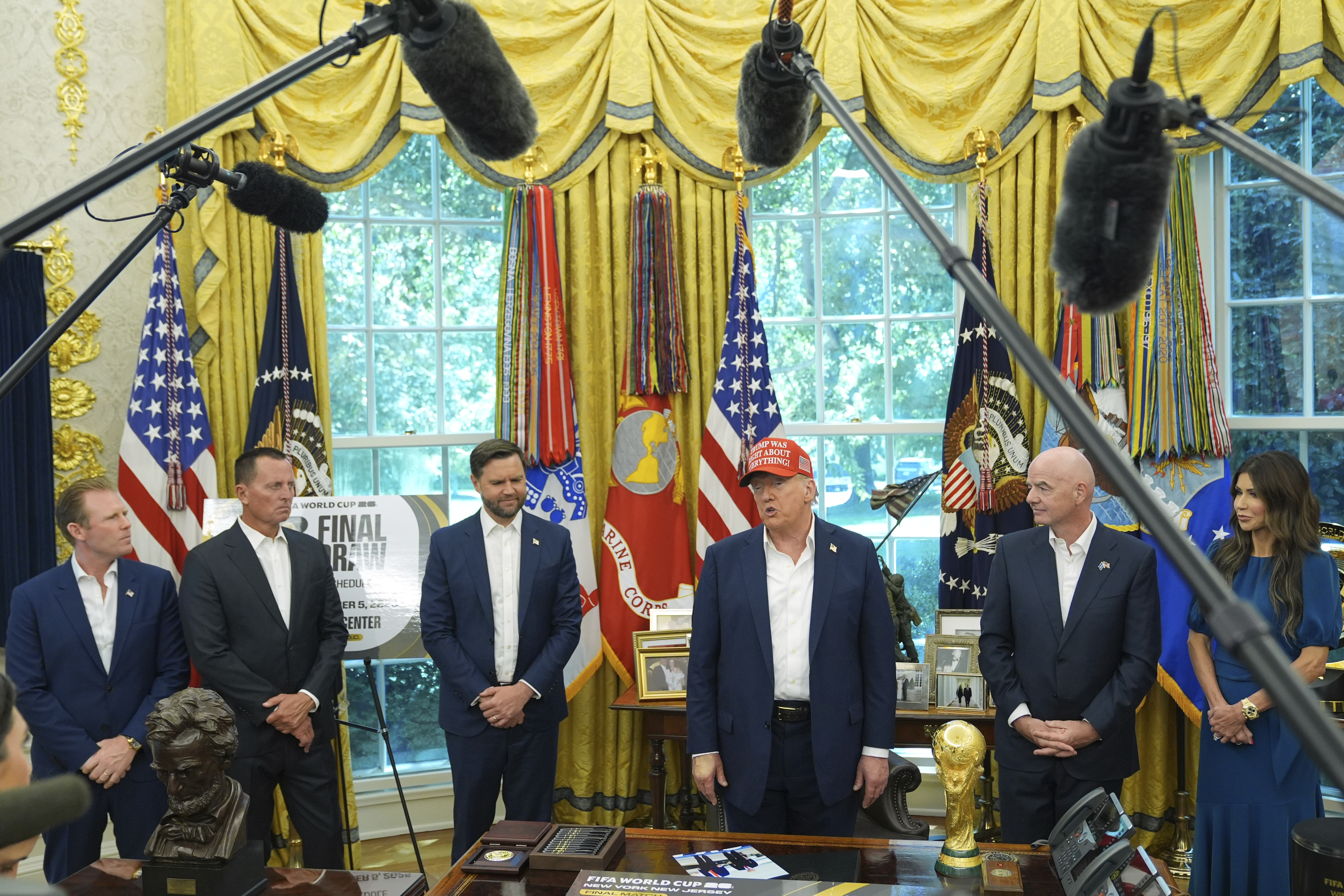Trump, Gianni Infantino and members of Trump's staff stand in the Oval Office surrounded by boom mics and reporters.