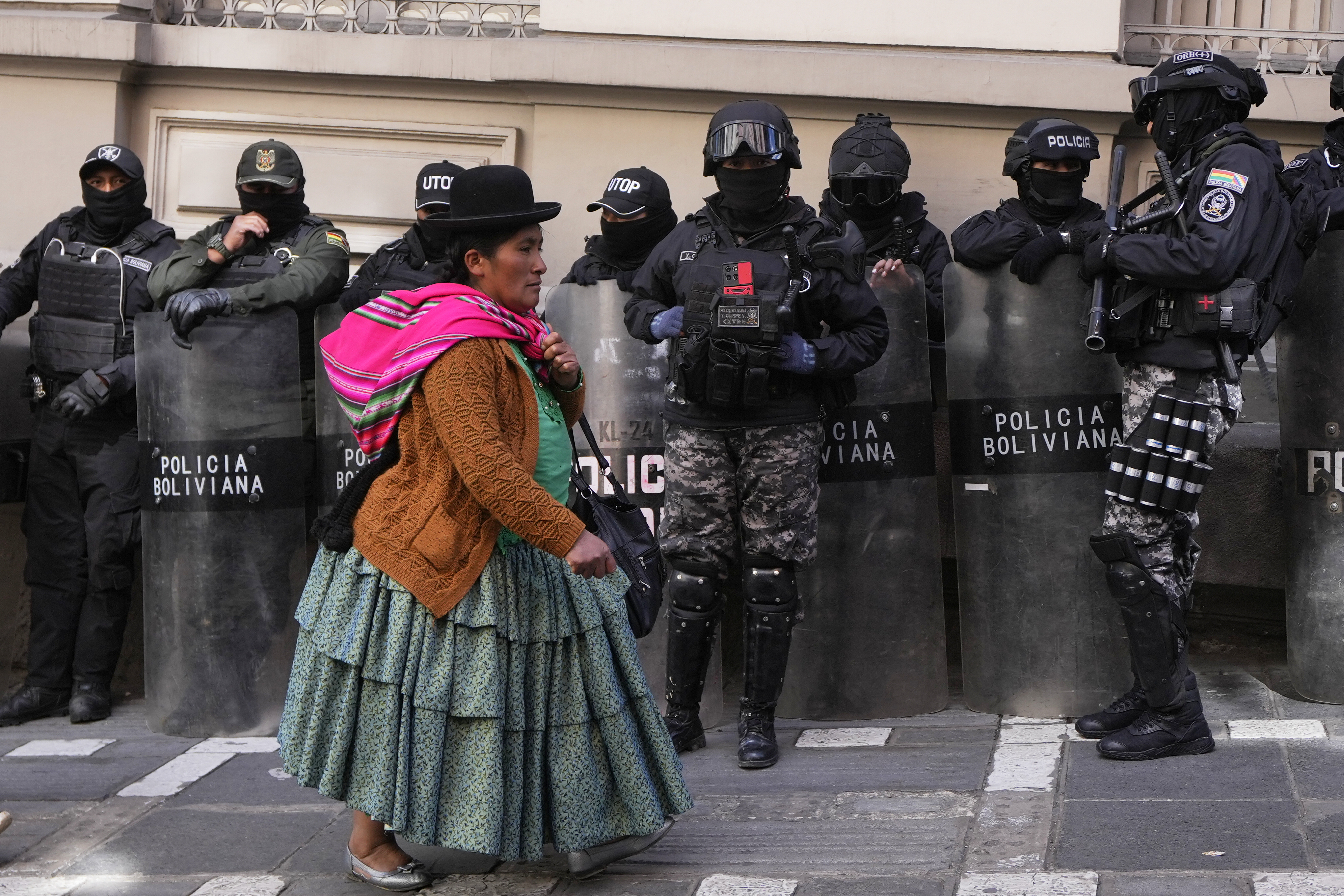 An Indigenous woman in Bolivia walks past police in riot gear