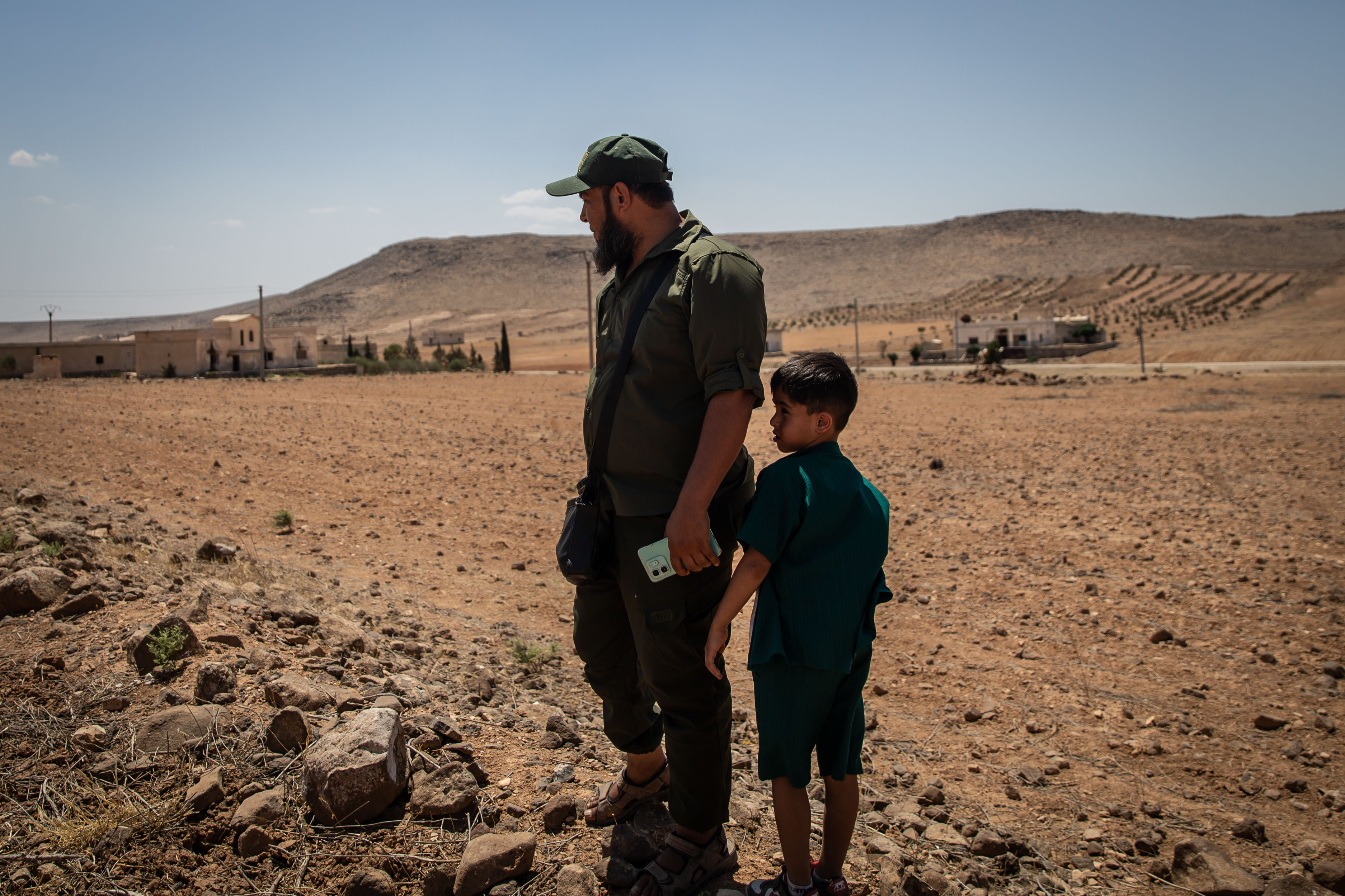 A man stands next to his son in an empty brown field 