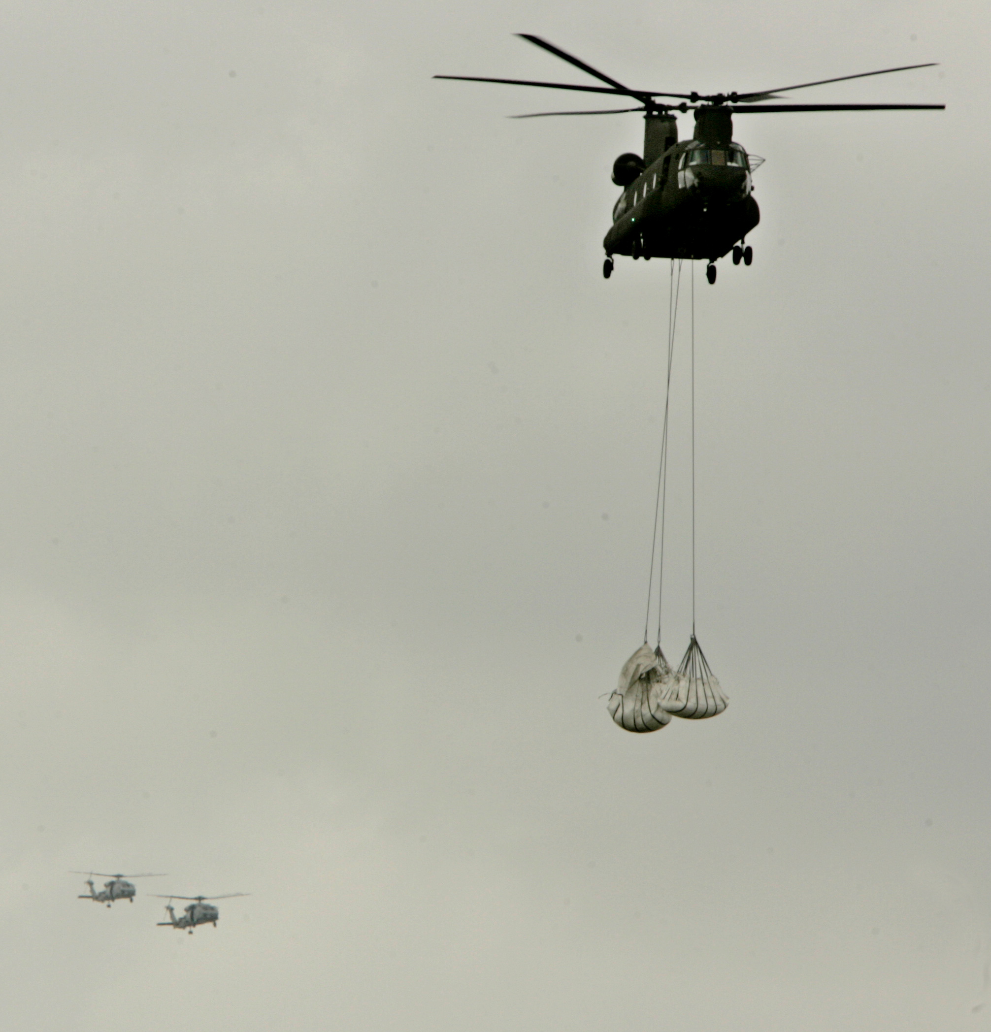 A military helicopter carrying sand bags is followed by a pair of survey helicopters as the Army Corps of Engineers drops sand bags in an attempt to shore up a breached levee along the industrial canal in New Orleans Saturday, Sept. 24, 2005. A breach in the levee along the canal caused water to spill back into the deserted ninth ward neighborhood which was flooded by Hurricane Katrina and had since dried out. (AP Photo/Charlie Riedel)