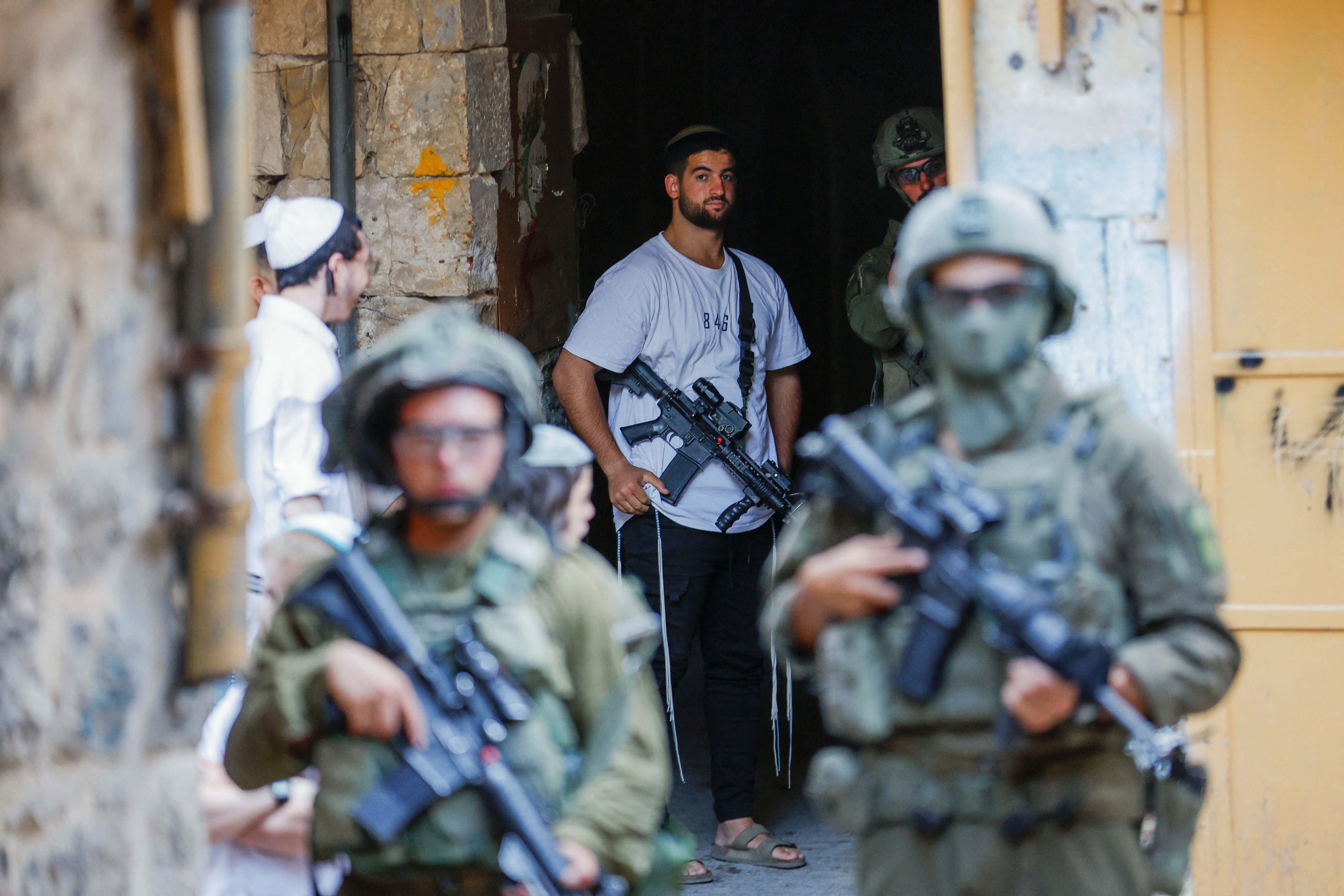 An armed settler stands near Israeli troops during a weekly settlers' tour in Hebron, in the Ioccupied West Bank,