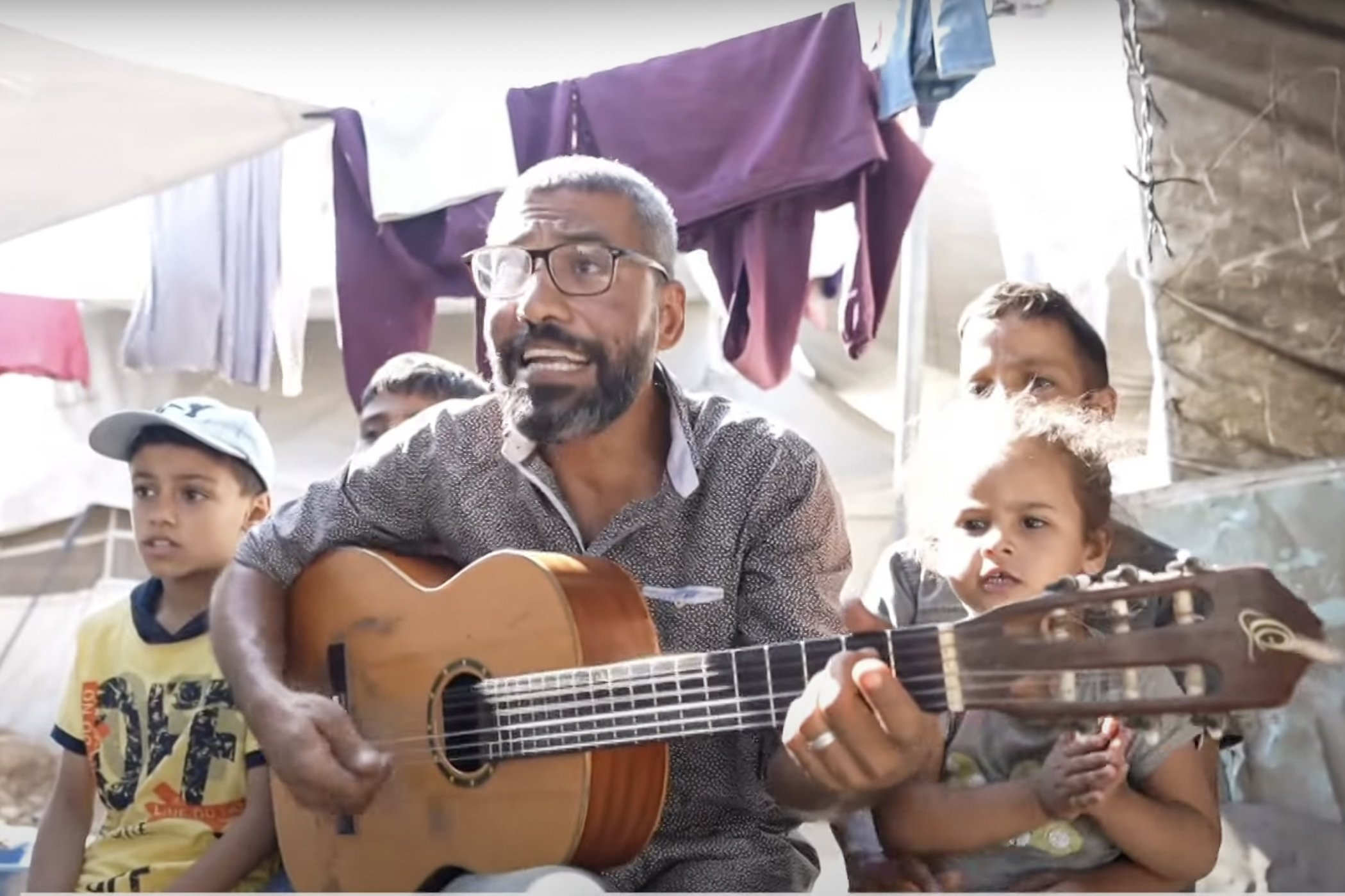 Musician Ahmad Abu Amsha sings with children in a makeshift camp in Gaza. 