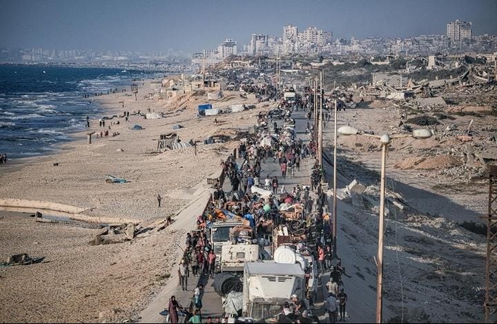 a photo of people fleeing on a coastal road with Gaza city behind them