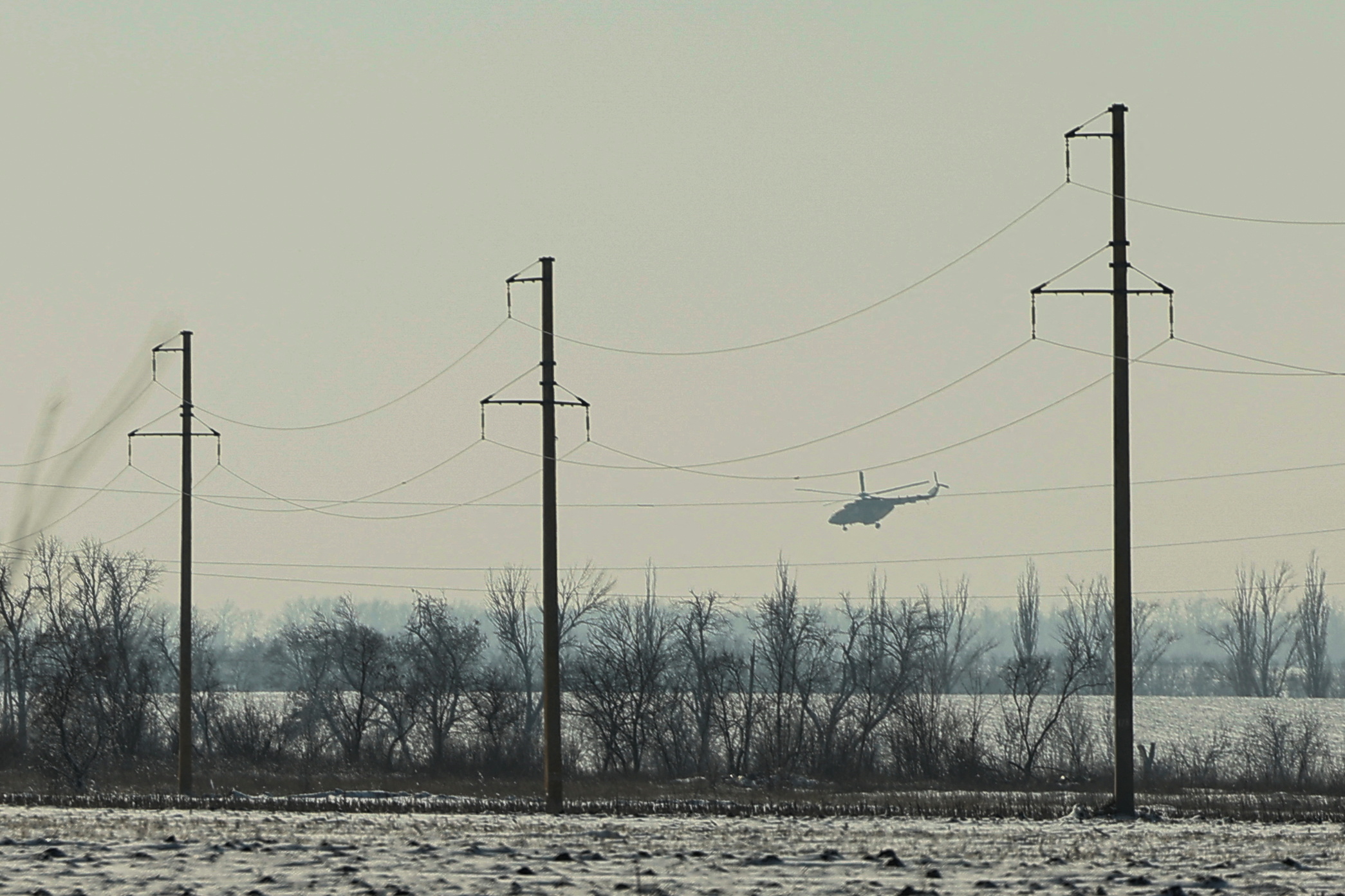 A military helicopter flies over a field.