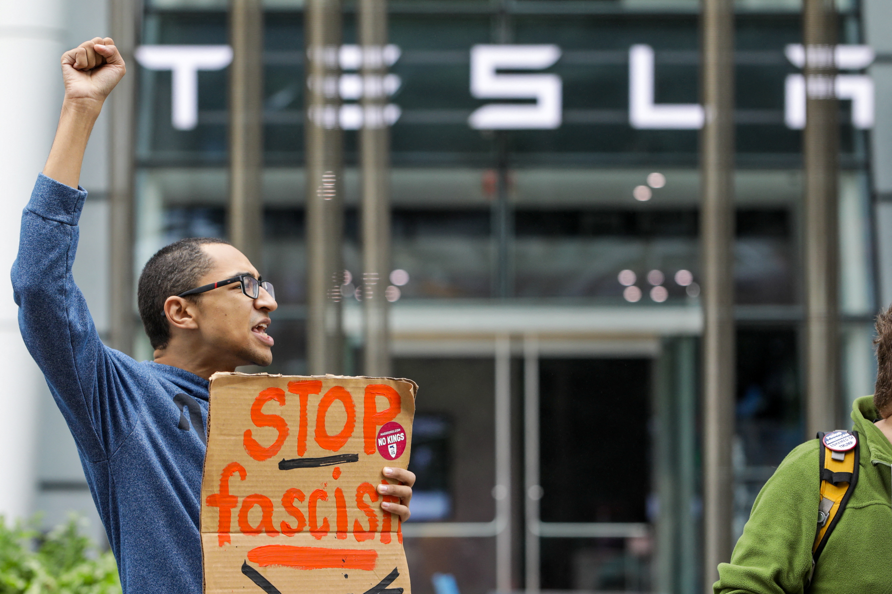 A protester holds a "stop fascist" sign outside of a Tesla dealership.