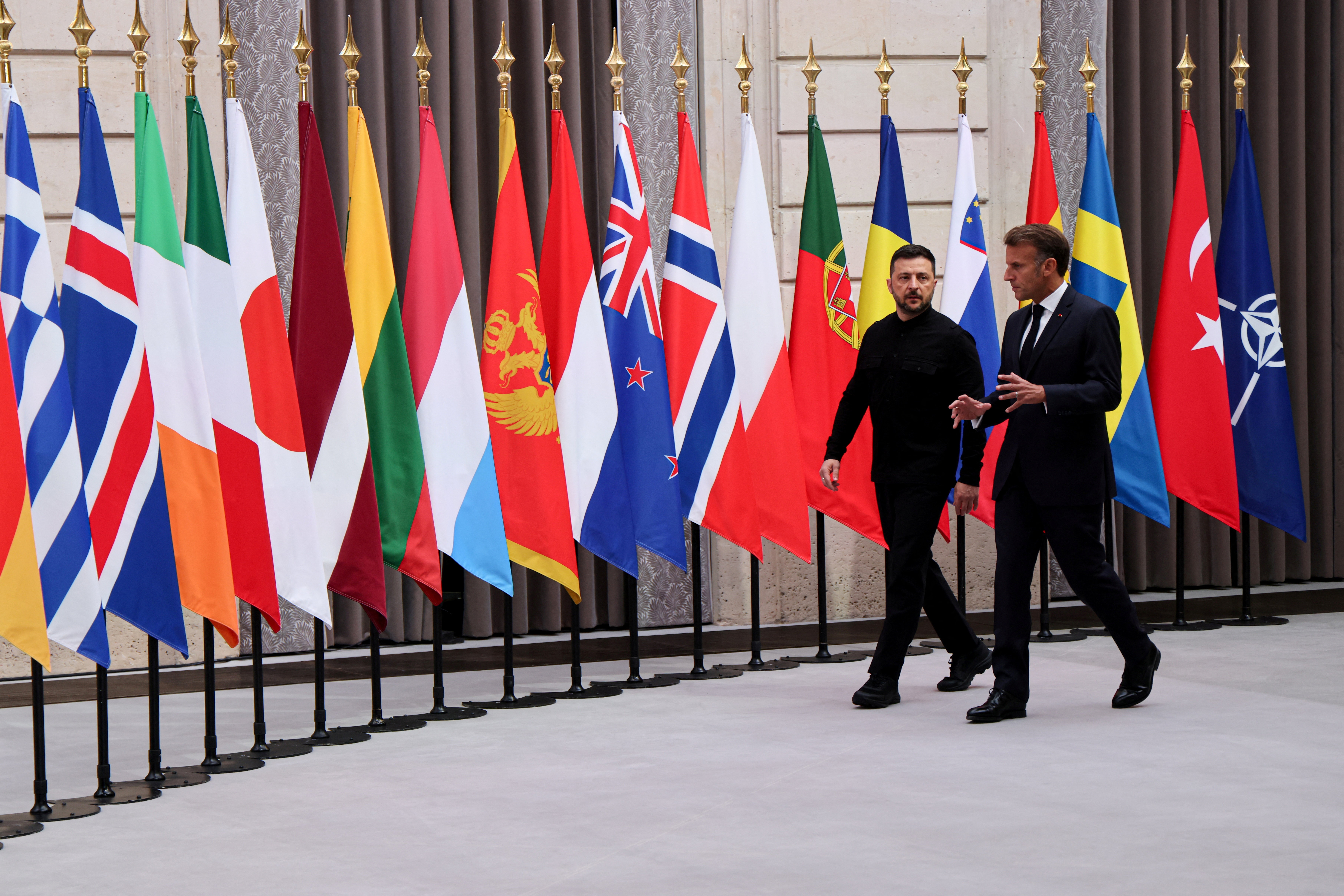 French President Emmanuel Macron and Ukrainian President Volodymyr Zelenskyy walk together, past flags.
