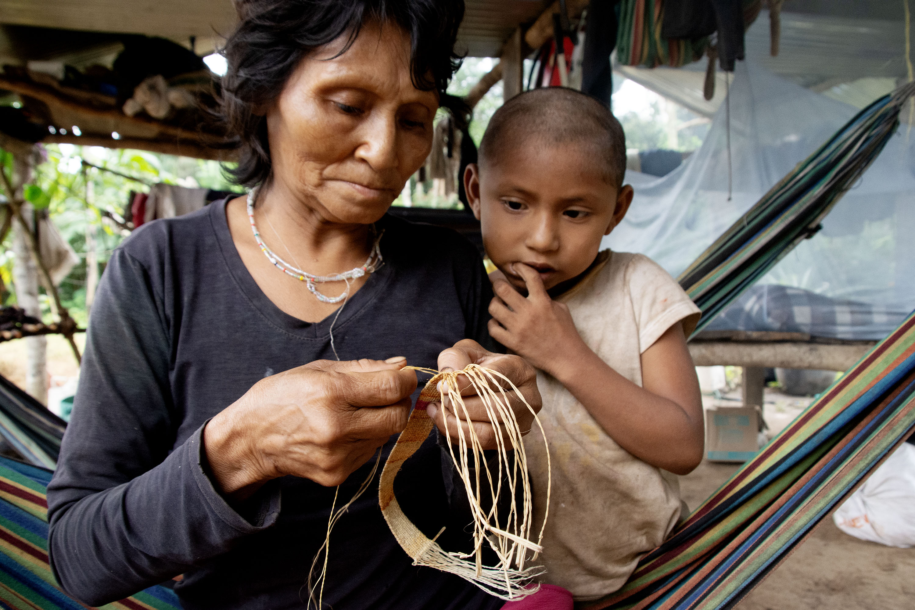 A woman weaves a bracelet out of palm fibers while a young girl looks on.