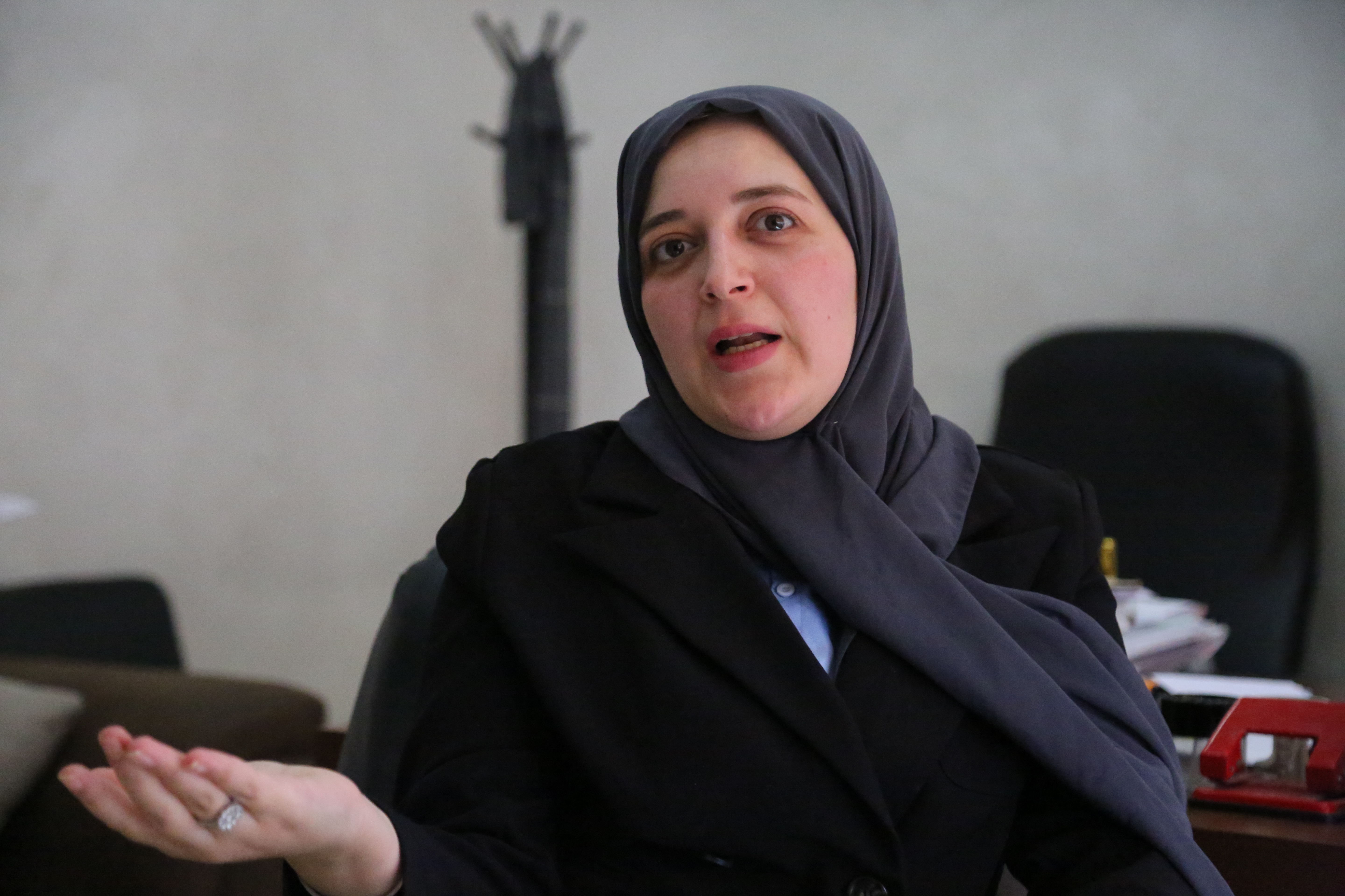 Kind-looking woman in a grey hijab gestures as she speaks