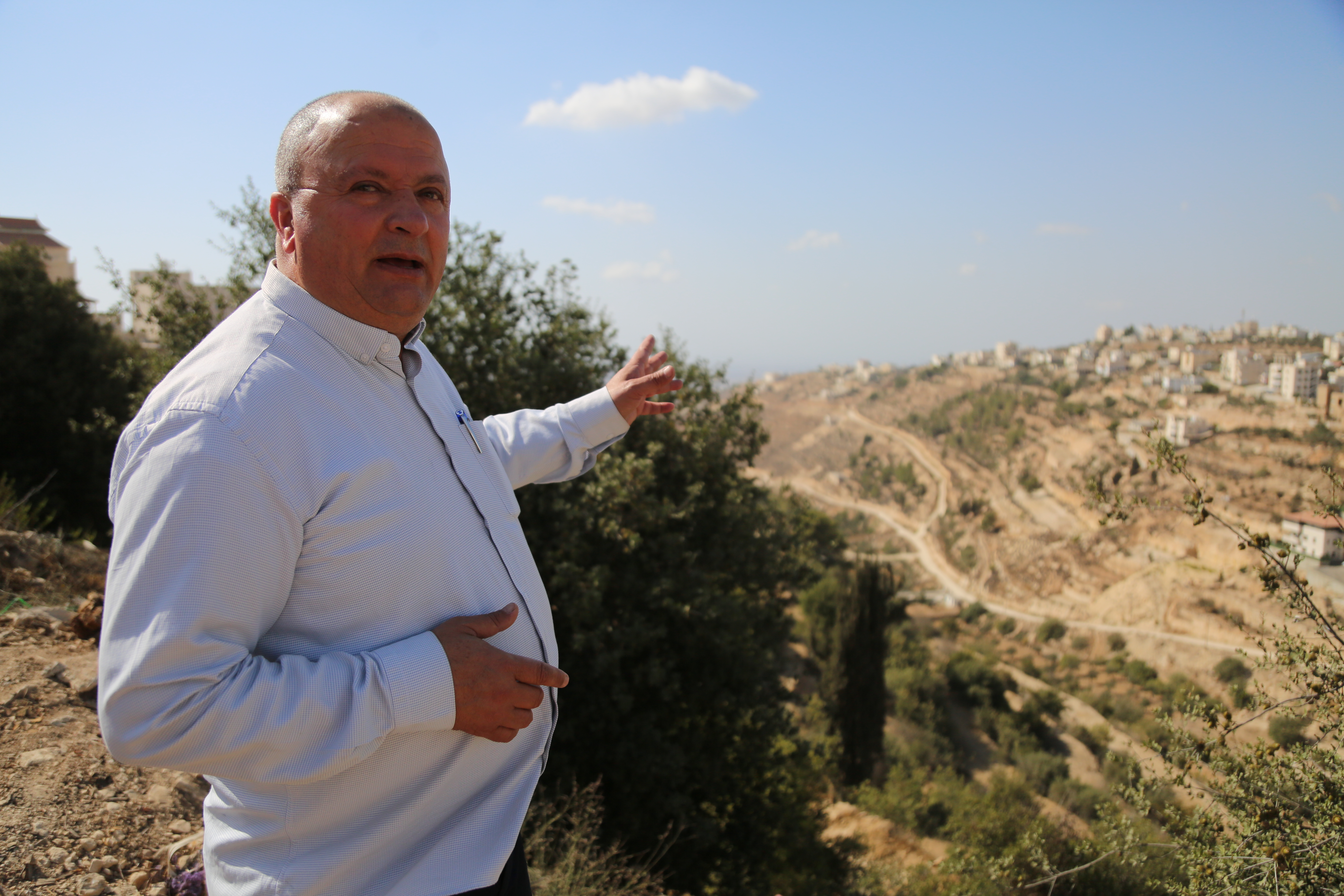 Jovial-looking bald man standing in the breeze on a hillside, gesturing as he speaks