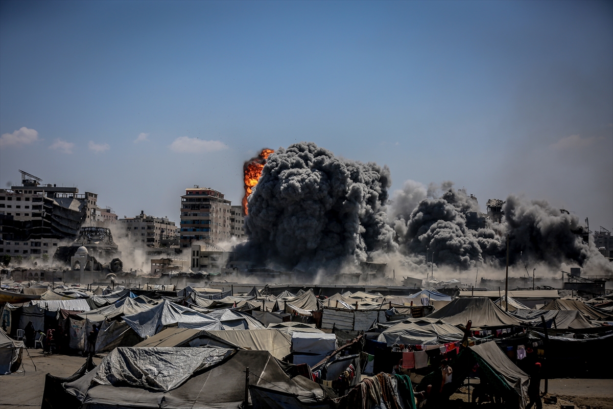 big clouds of grey dust rise from a destroyed apartment building with rows and rows of tents in the foreground