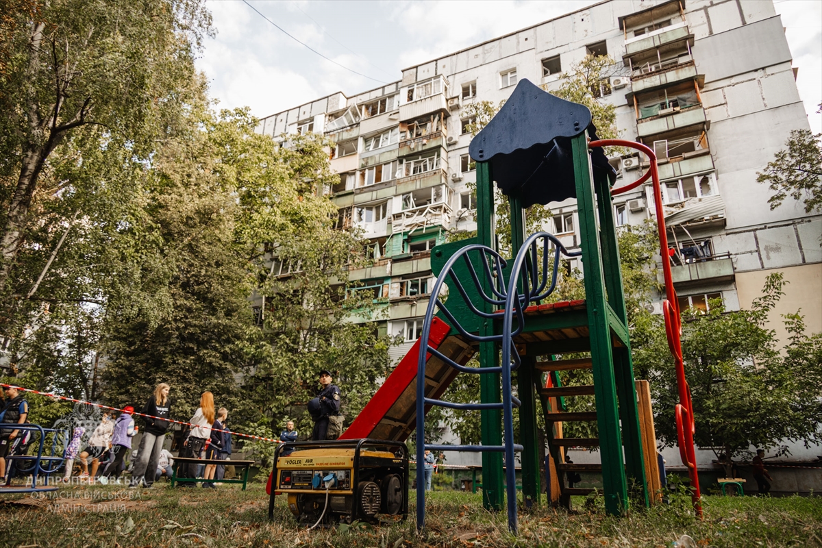 people stand in a play ground next to a damaged apartment complex