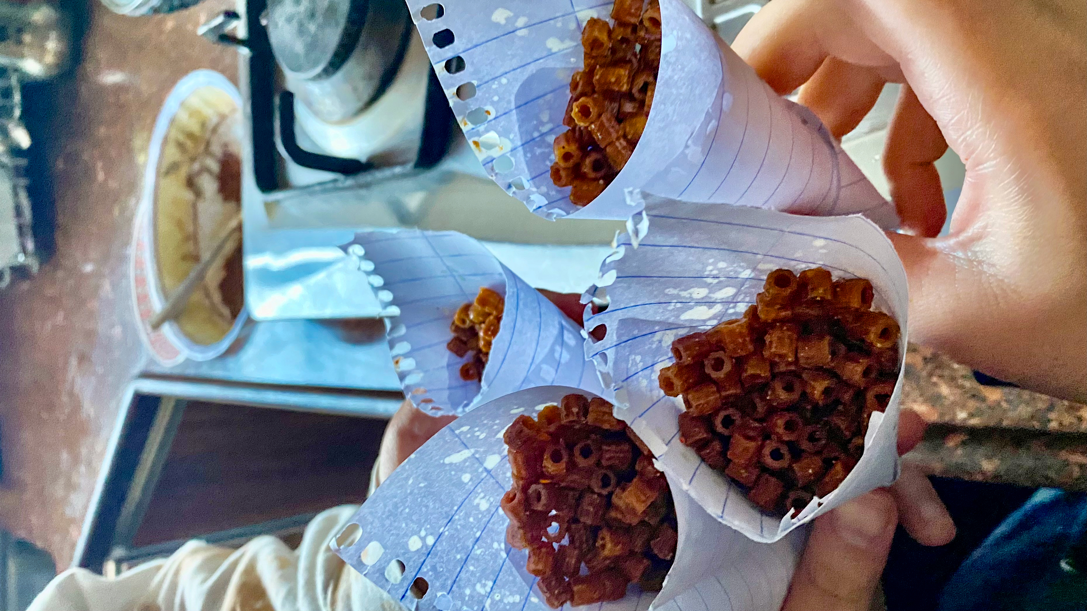 Four cones made of notebook paper, filled with fried and spiced macaroni.