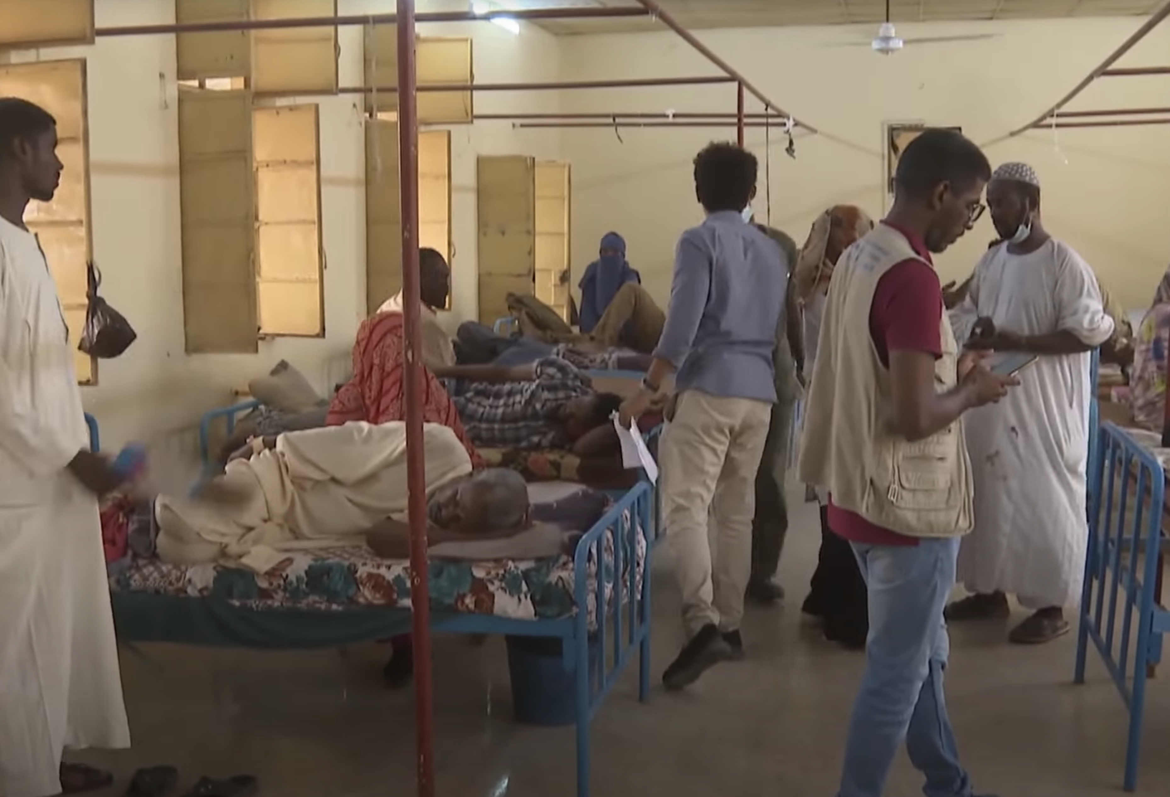 A crowded hospital ward with patients and staff.