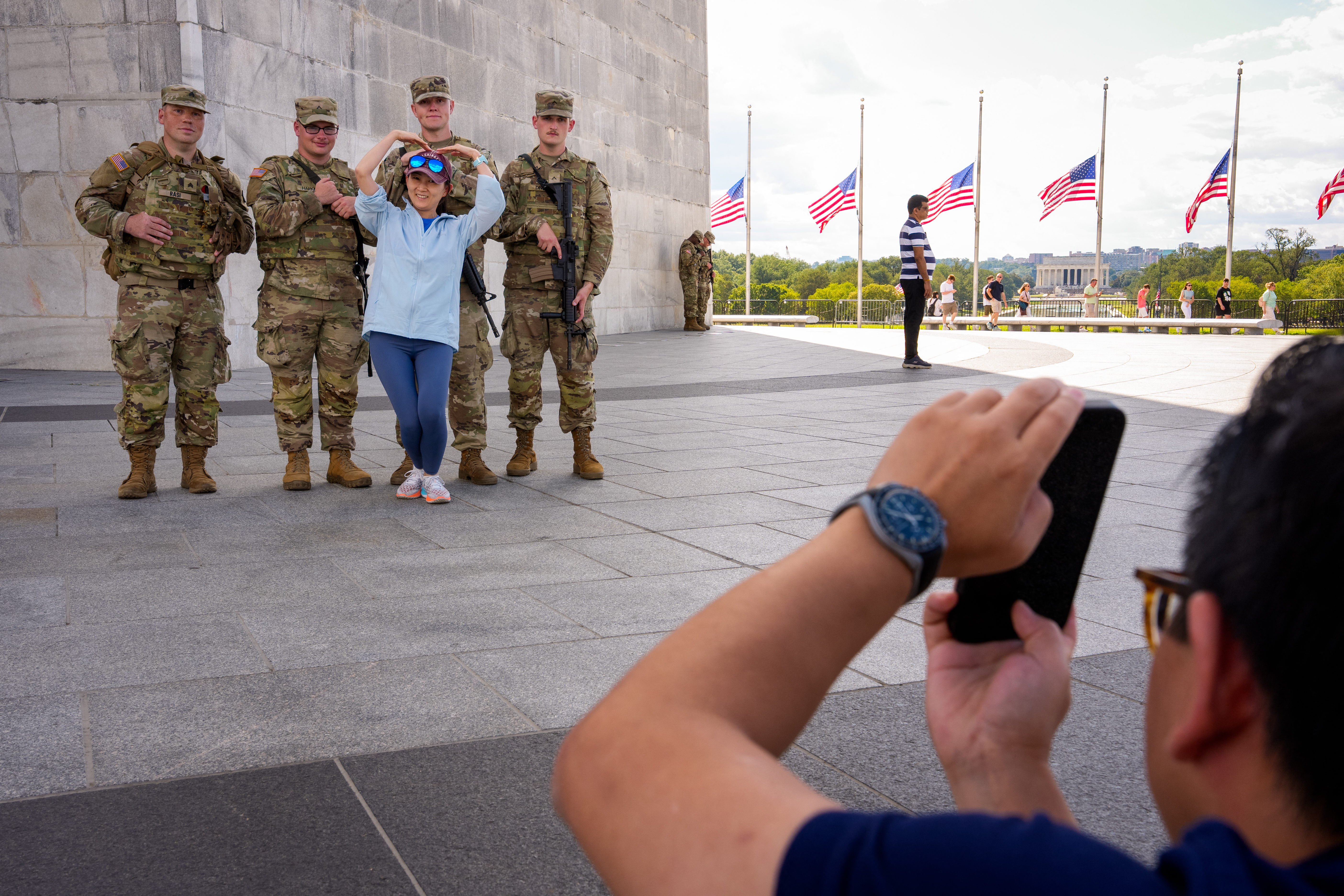 WASHINGTON, DC - AUGUST 27: A tourist visiting from Shenzhen, China, poses for a photograph with armed members of the National Guard at the base of the Washington on the National Mall on August 27, 2025 in Washington, DC. The Trump administration has deployed federal officers and the National Guard to the District in order to place the DC Metropolitan Police Department under federal control and assist in crime prevention in the nation's capital. Andrew Harnik/Getty Images/AFP (Photo by Andrew Harnik / GETTY IMAGES NORTH AMERICA / Getty Images via AFP)