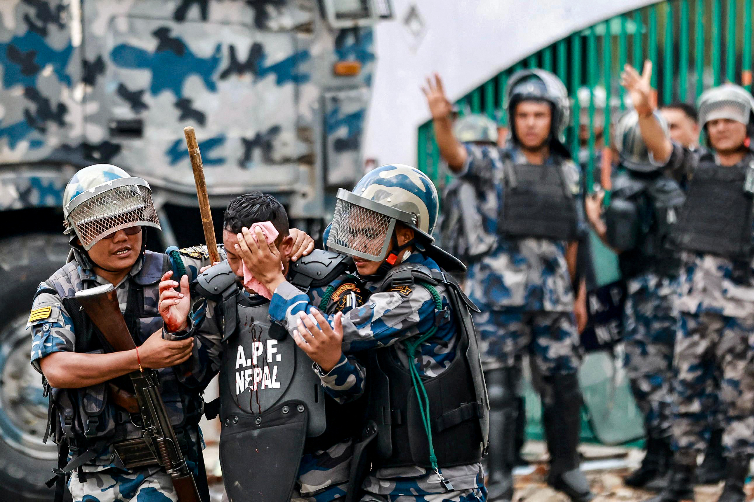 TOPSHOT - Riot police personnel carry an injured comrade as demonstrators pelt stones during a protest outside the Parliament in Kathmandu on September 8, 2025, condemning social media prohibitions and corruption by the government.