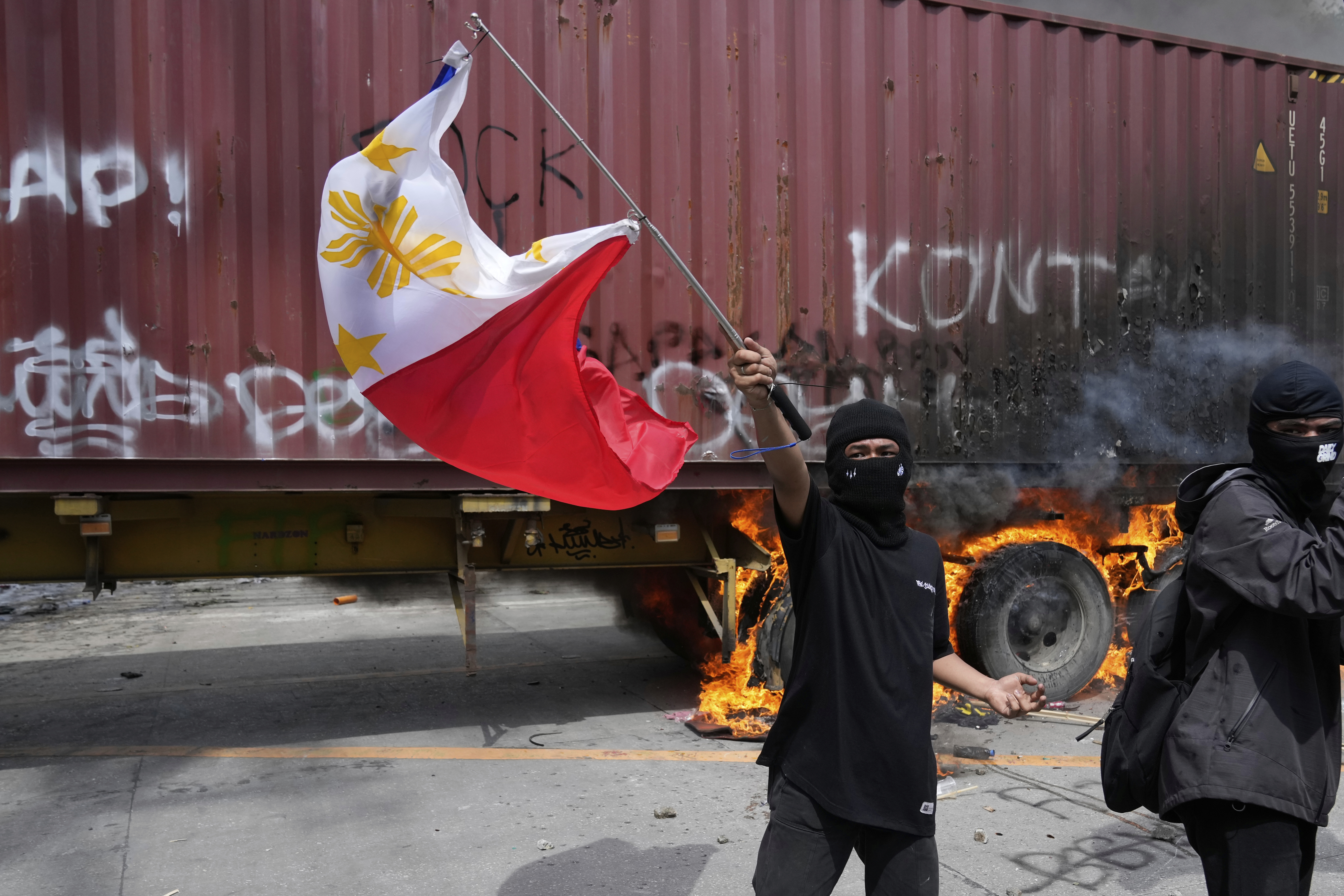 A protester waves a Philippine flag beside a burning truck following clashes with police as they tried to enter the Malacanang presidential palace compound in Manila, Philippines on Sunday, Sept. 21, 2025. (AP Photo/Aaron Favila)
