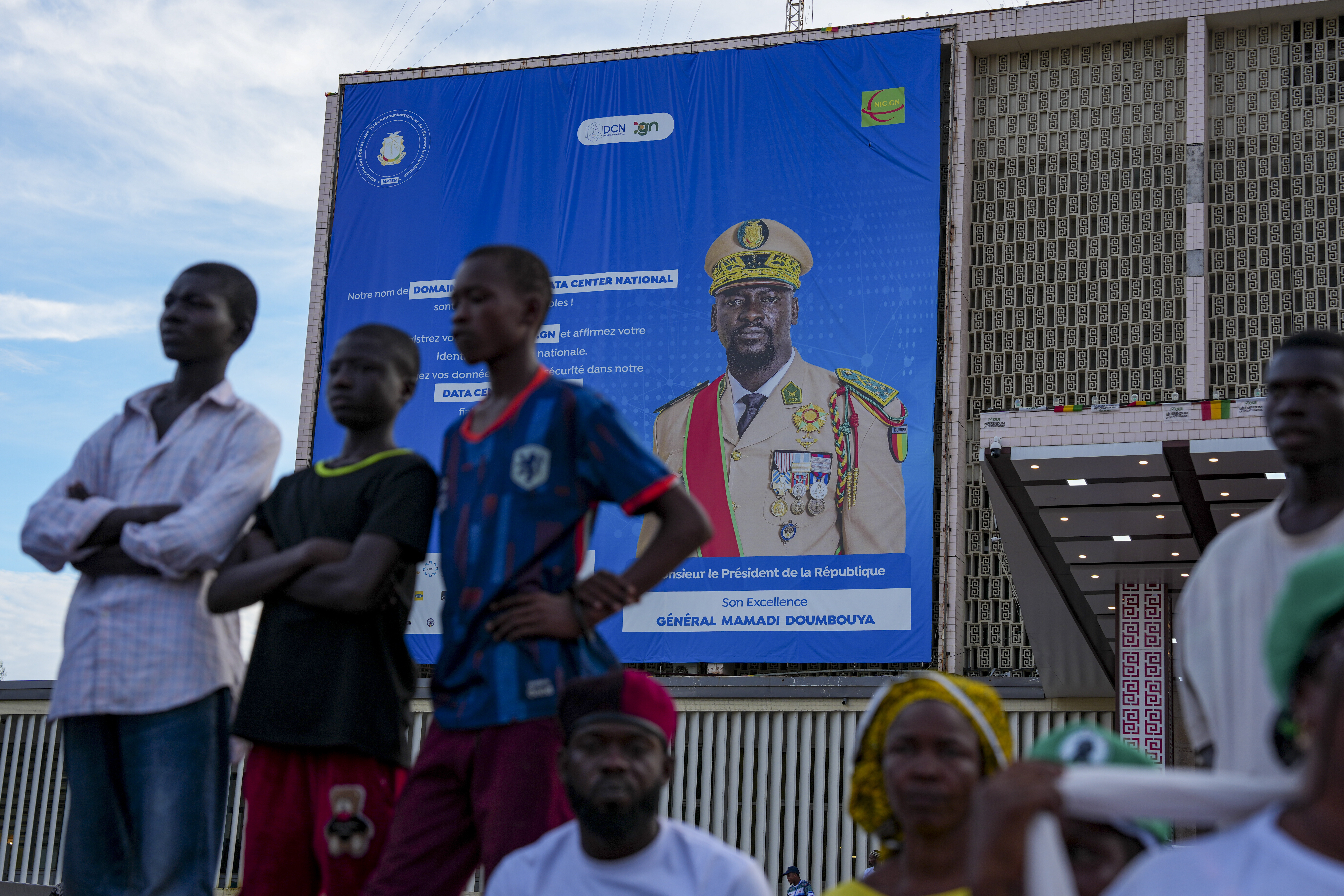 CORRECTS TITLE OF MILITARY LEADER People stand in front of a billboard showing Guinea's interim President, Gen. Mamadi Doumbouya, ahead of the constitutional referendum in Conakry, Guinea, Thursday, Sept. 18, 2025. (AP Photo/Misper Apawu)